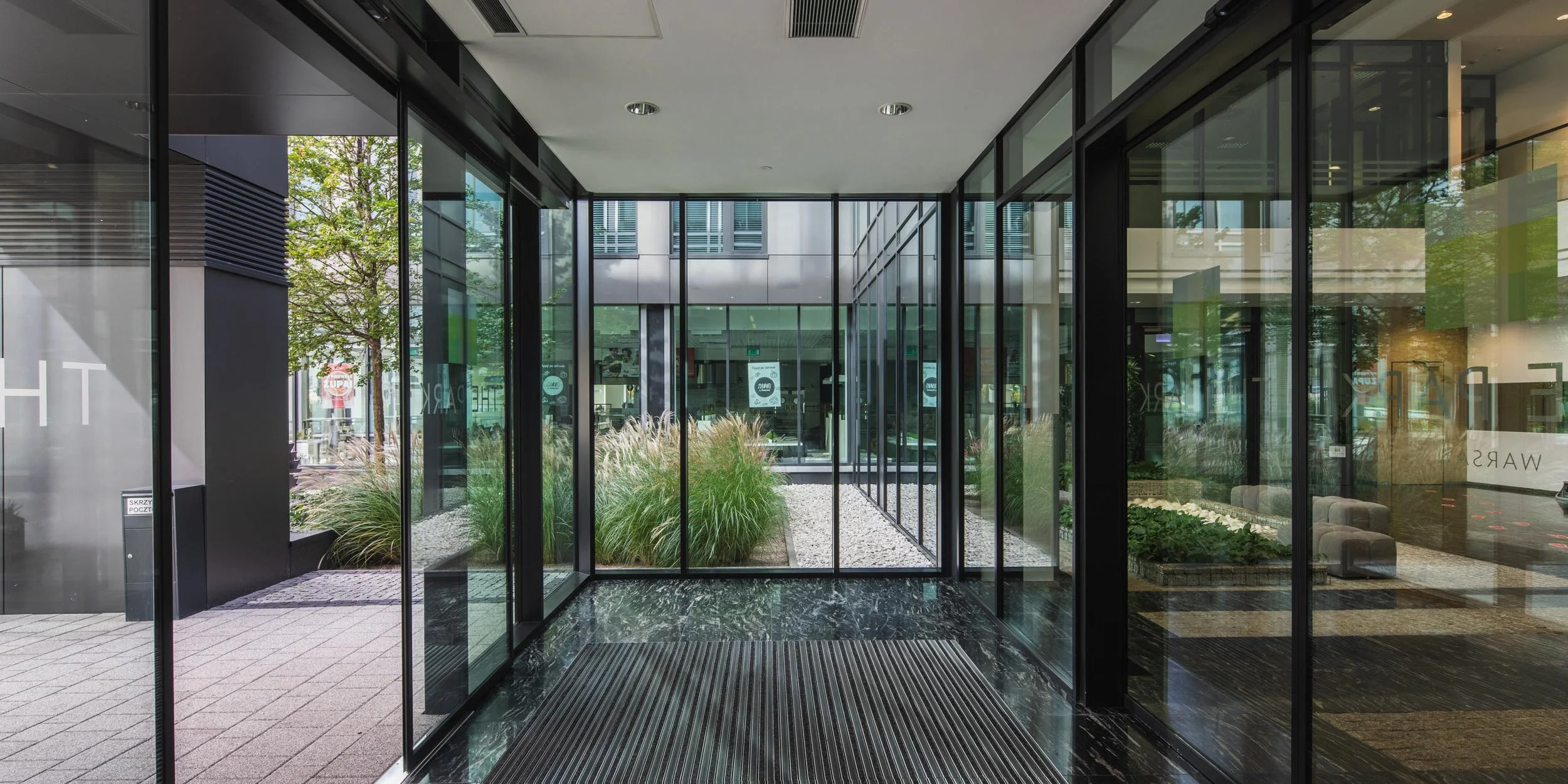 Modern glass entrance with indoor garden and view of city outside.