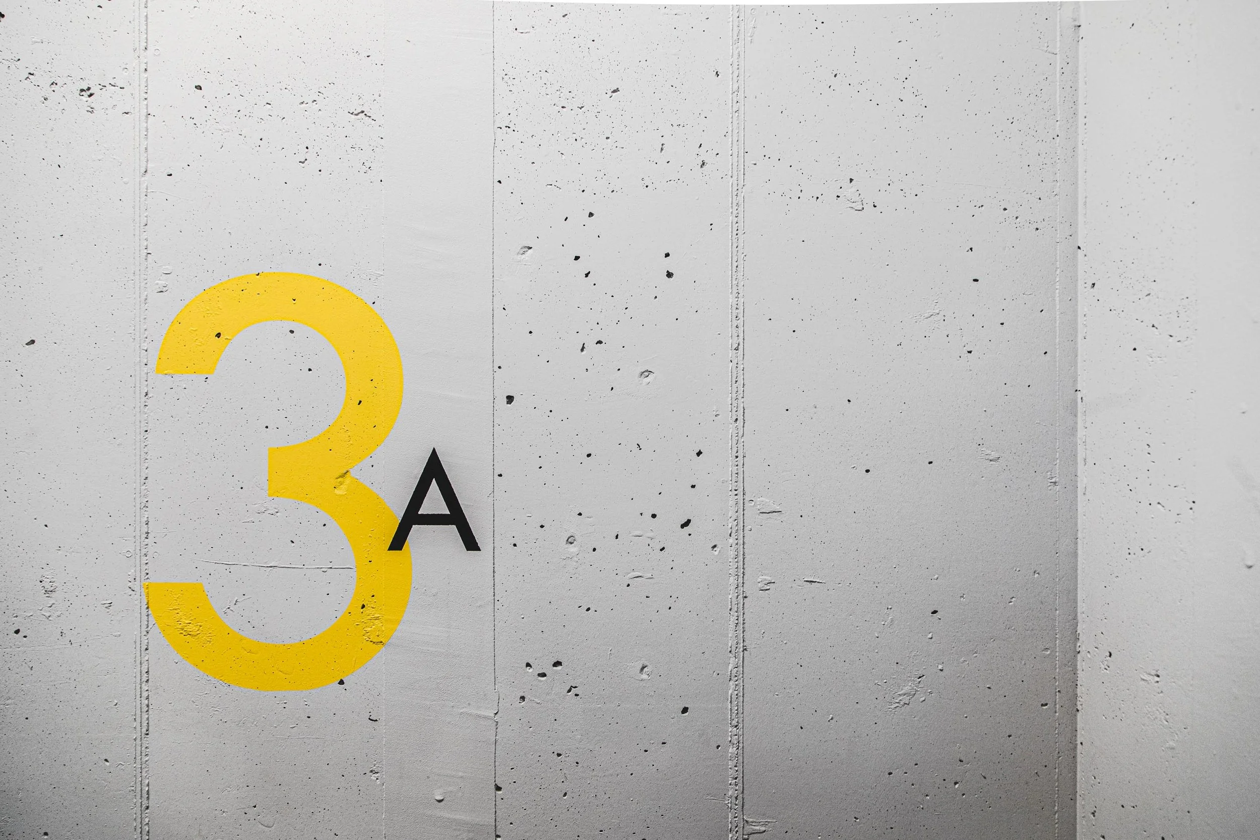Concrete wall with yellow number 3 and black letter A painted on it.