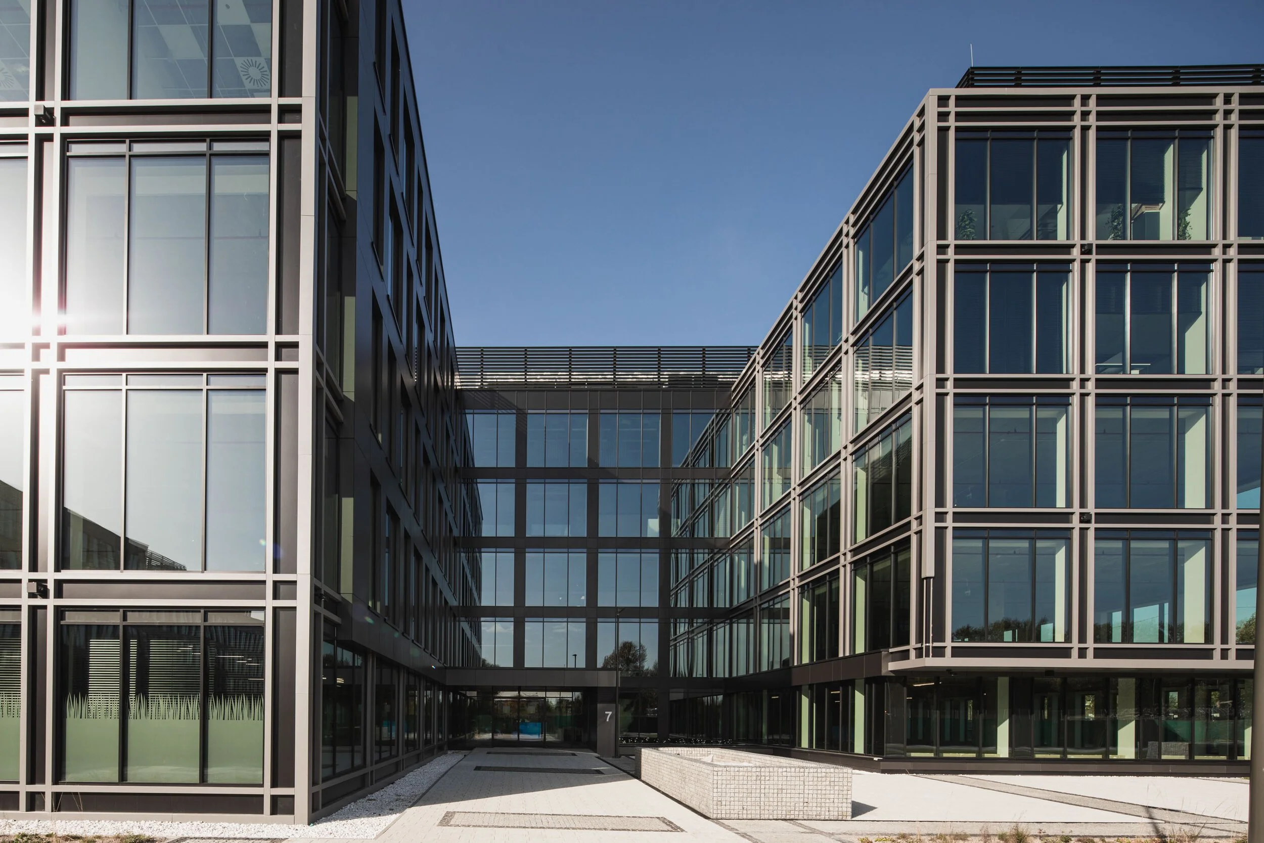 Modern glass and metal office building with a sky bridge connecting two sections, on a clear day.