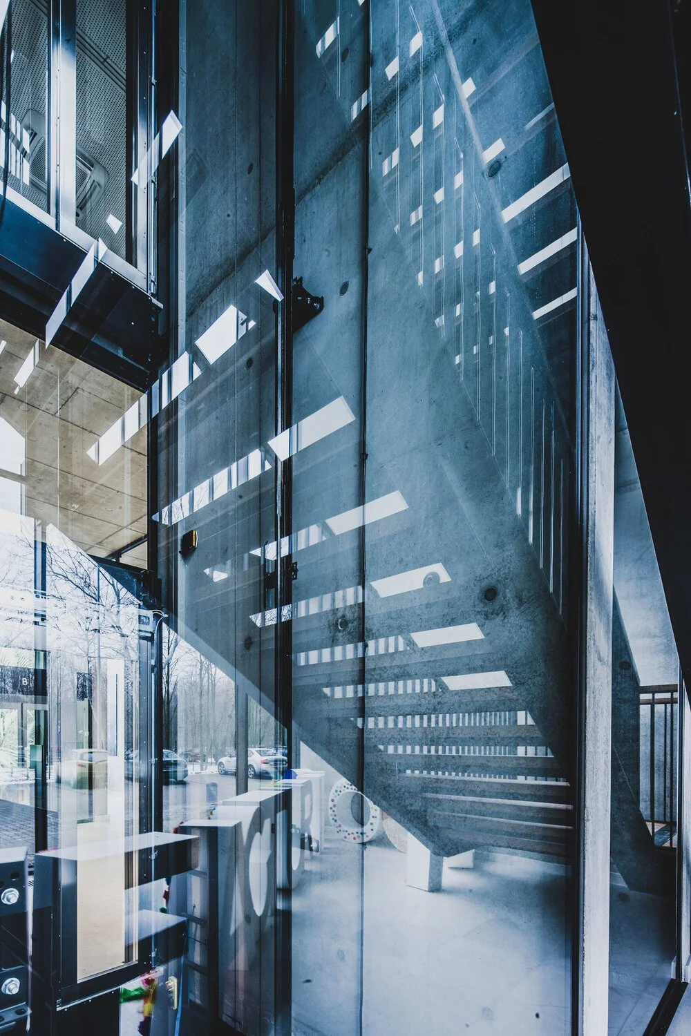 Interior of a modern building with glass walls, concrete staircase, and reflections of ceiling lights on the glass.