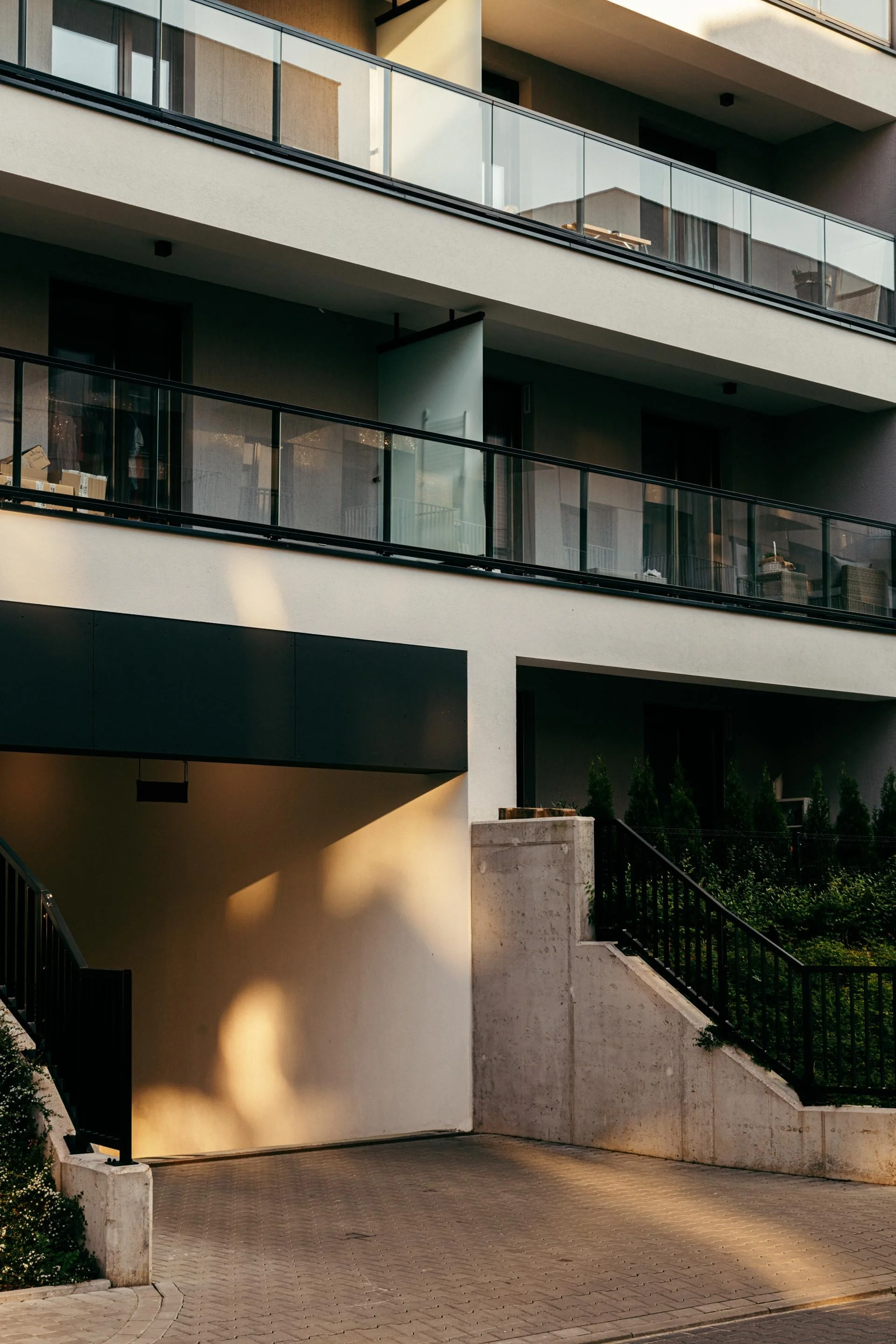 Modern residential building with multiple levels of balconies and glass railings, illuminated by warm sunlight.