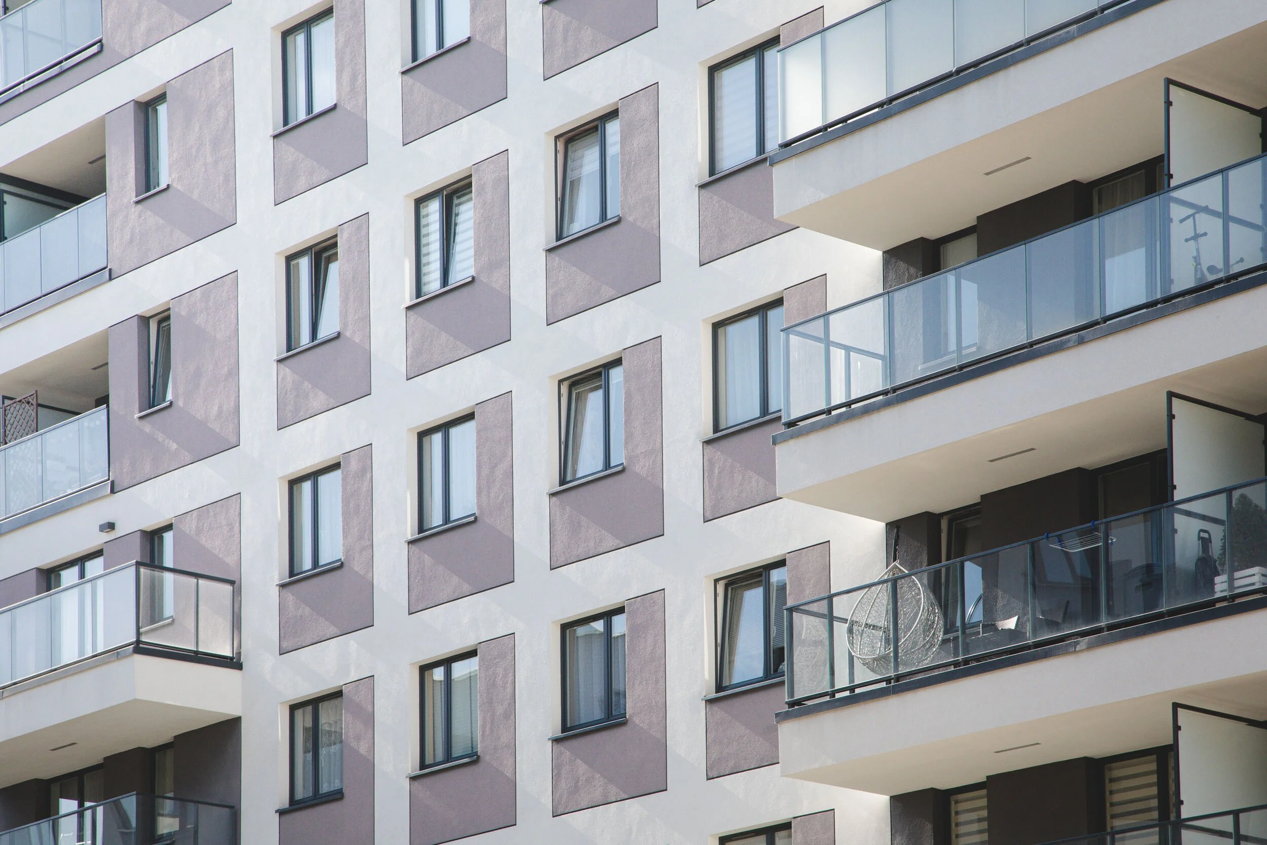 Facade of a modern apartment building with multiple windows and balconies, some with glass railings.
