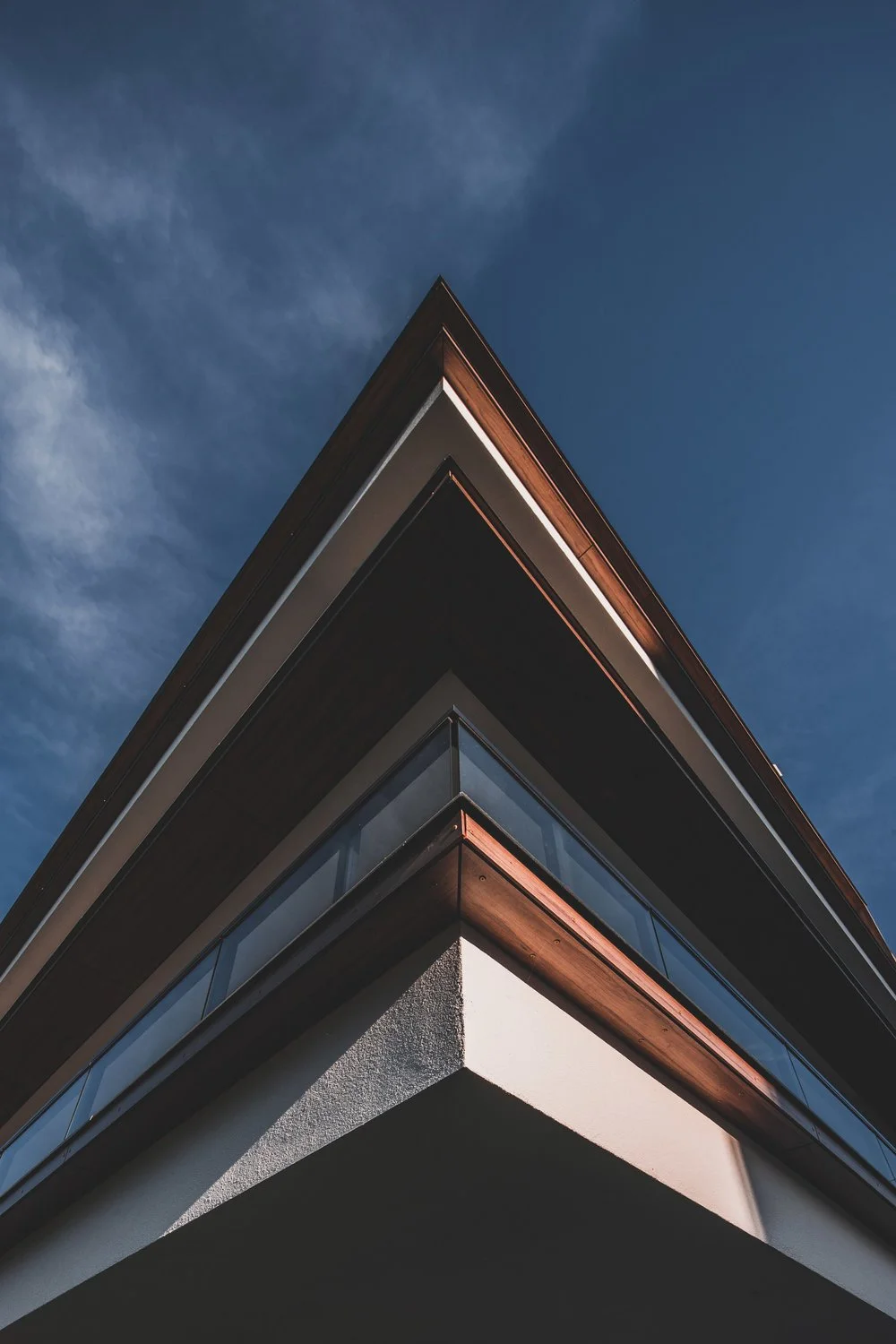 Low-angle view of a modern building with wood accents and glass balconies against a blue sky with wispy clouds.