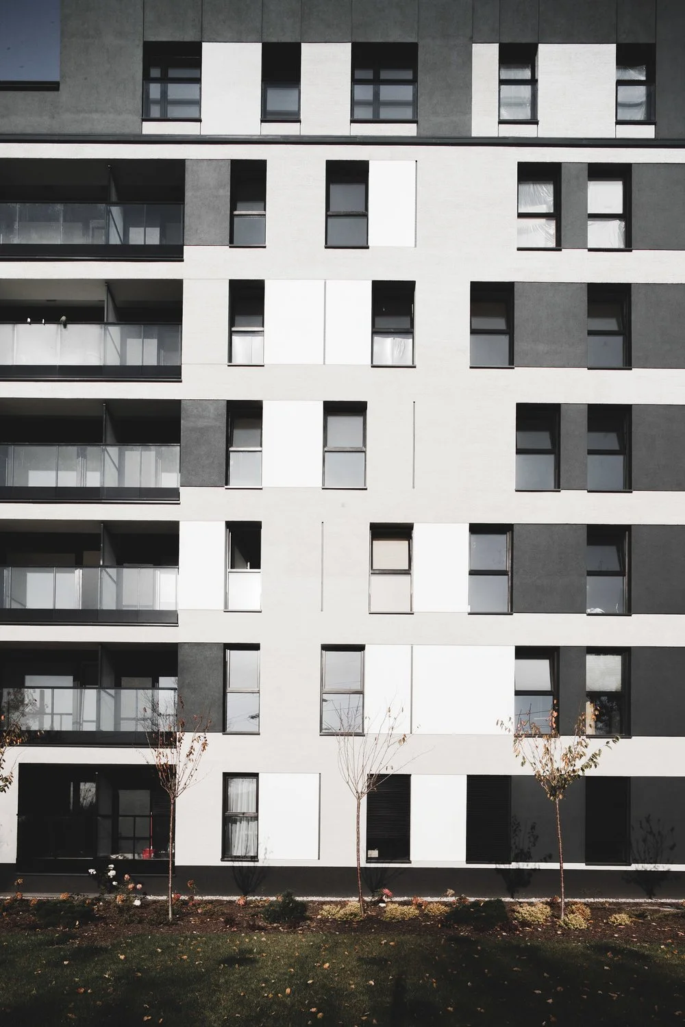 Modern multi-story apartment building with black and white window panels and small trees in front.