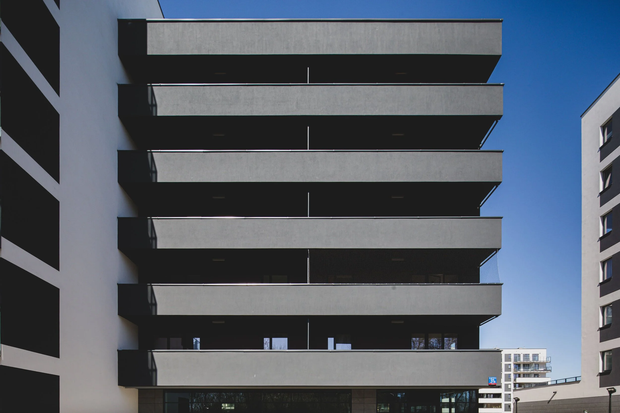 Modern gray apartment building with horizontal balconies, set against a clear blue sky.
