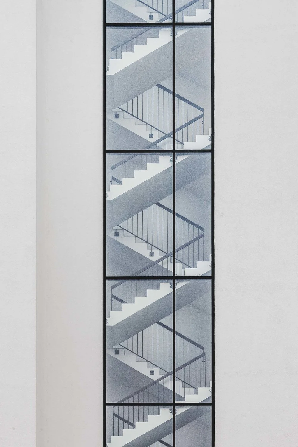 Photo of an elevator shaft with multiple visible staircases through glass windows, with white walls on either side.