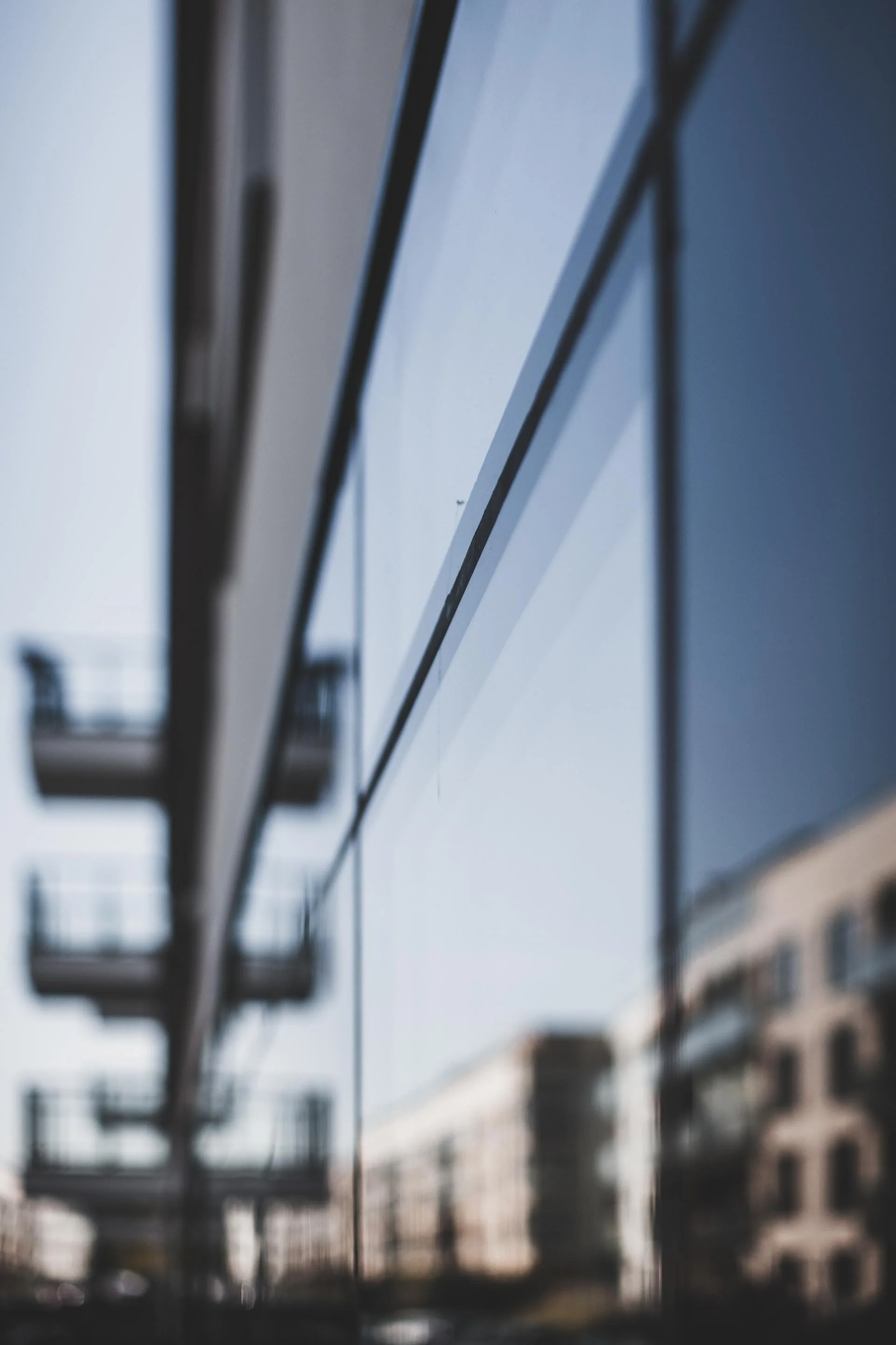 Close-up of a modern building's reflective glass facade, showing reflections of nearby buildings and a clear sky.