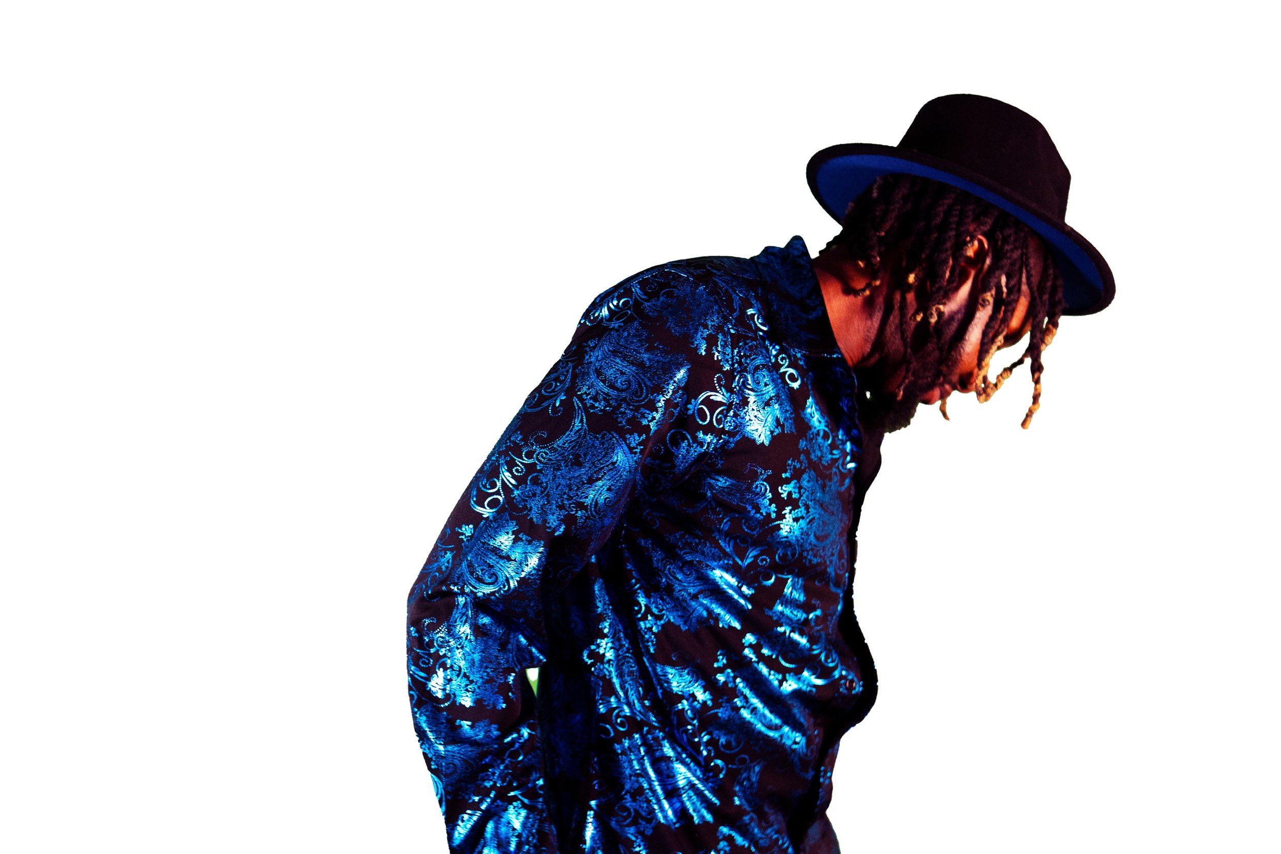 Person wearing a black hat and shiny blue patterned shirt against a white background.