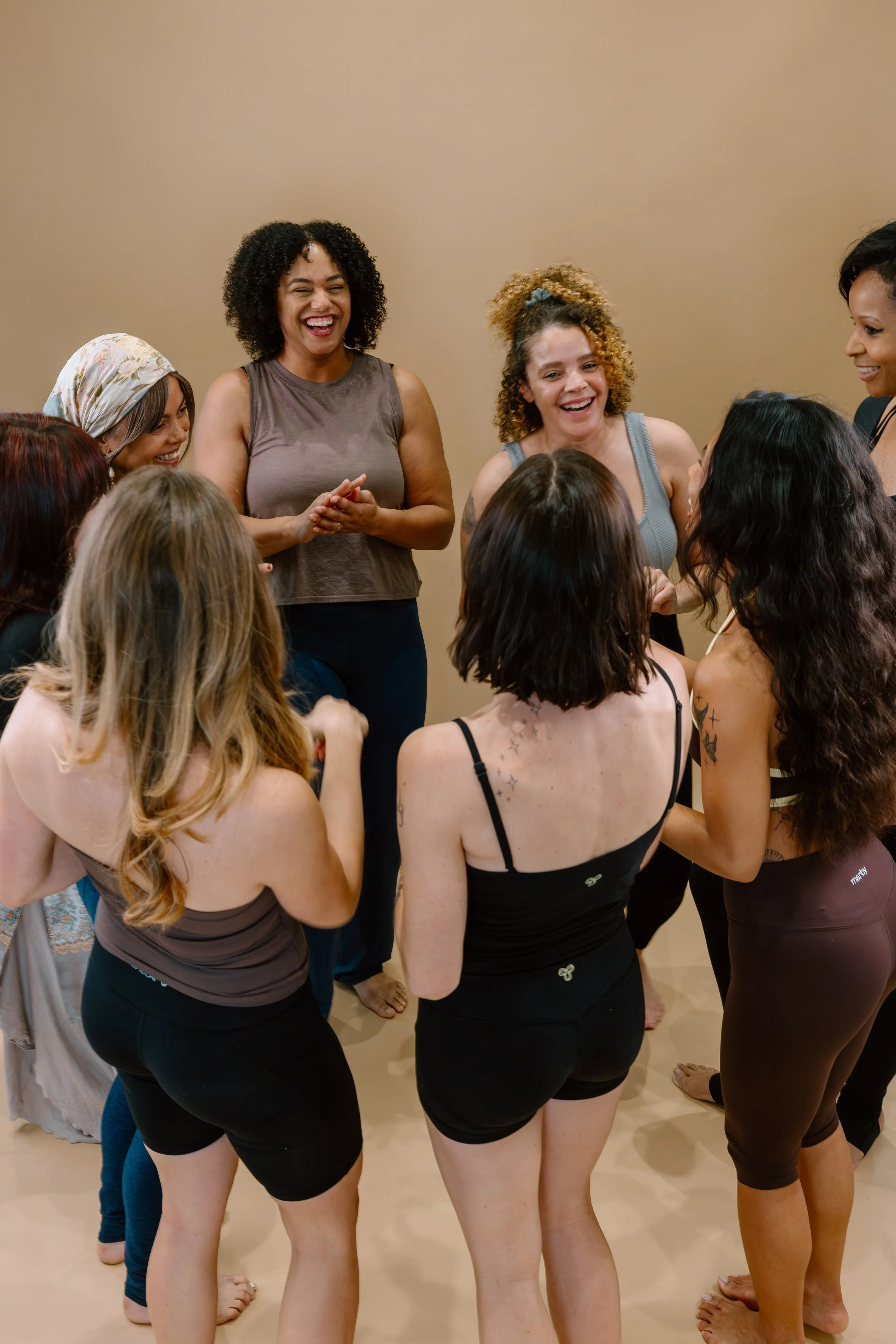 Group of women standing together in a circle, smiling and talking indoors.