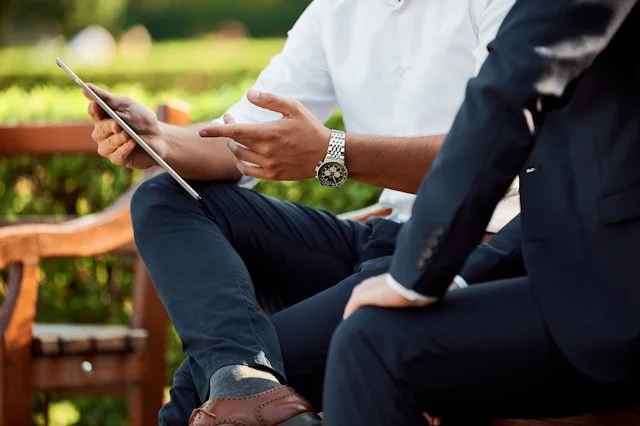Two men in business attire discussing content on a tablet outdoors.