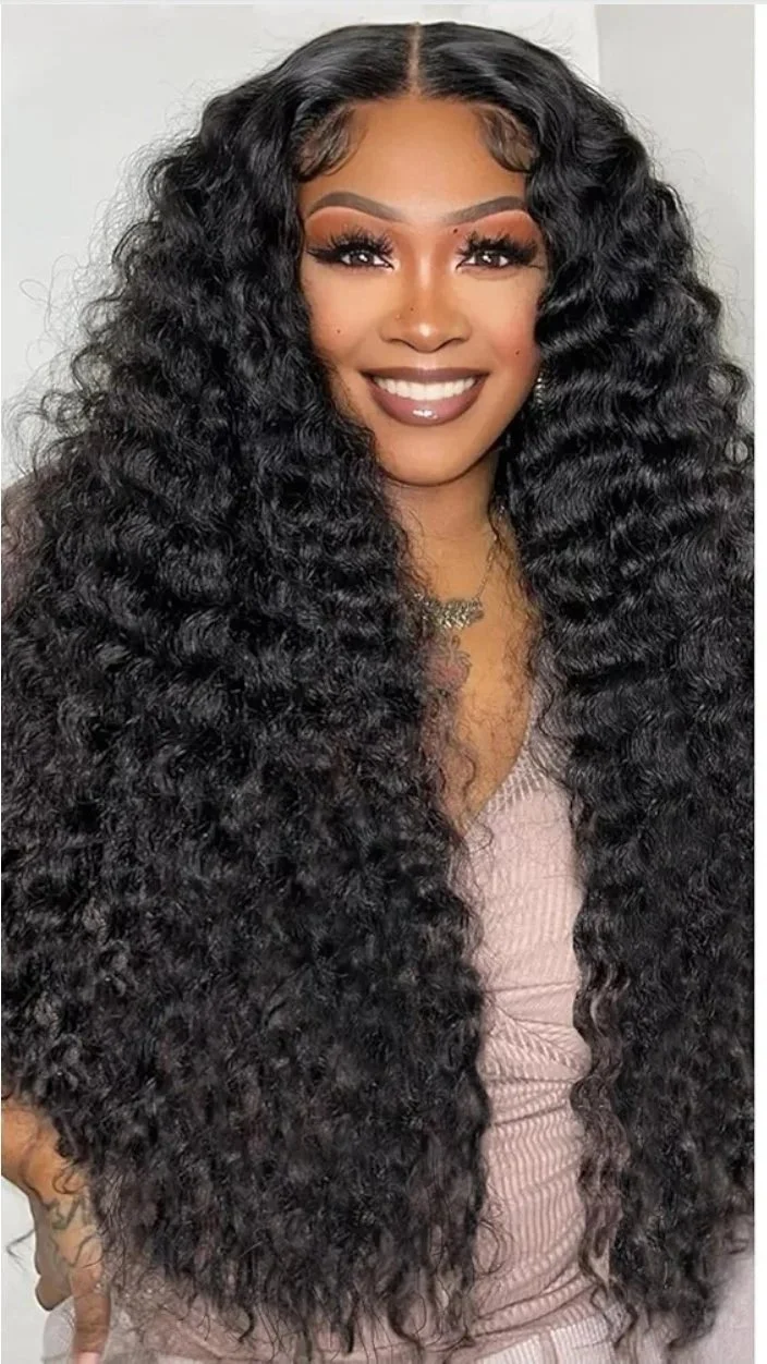Woman with long, curly black hair, smiling, wearing makeup and jewelry.