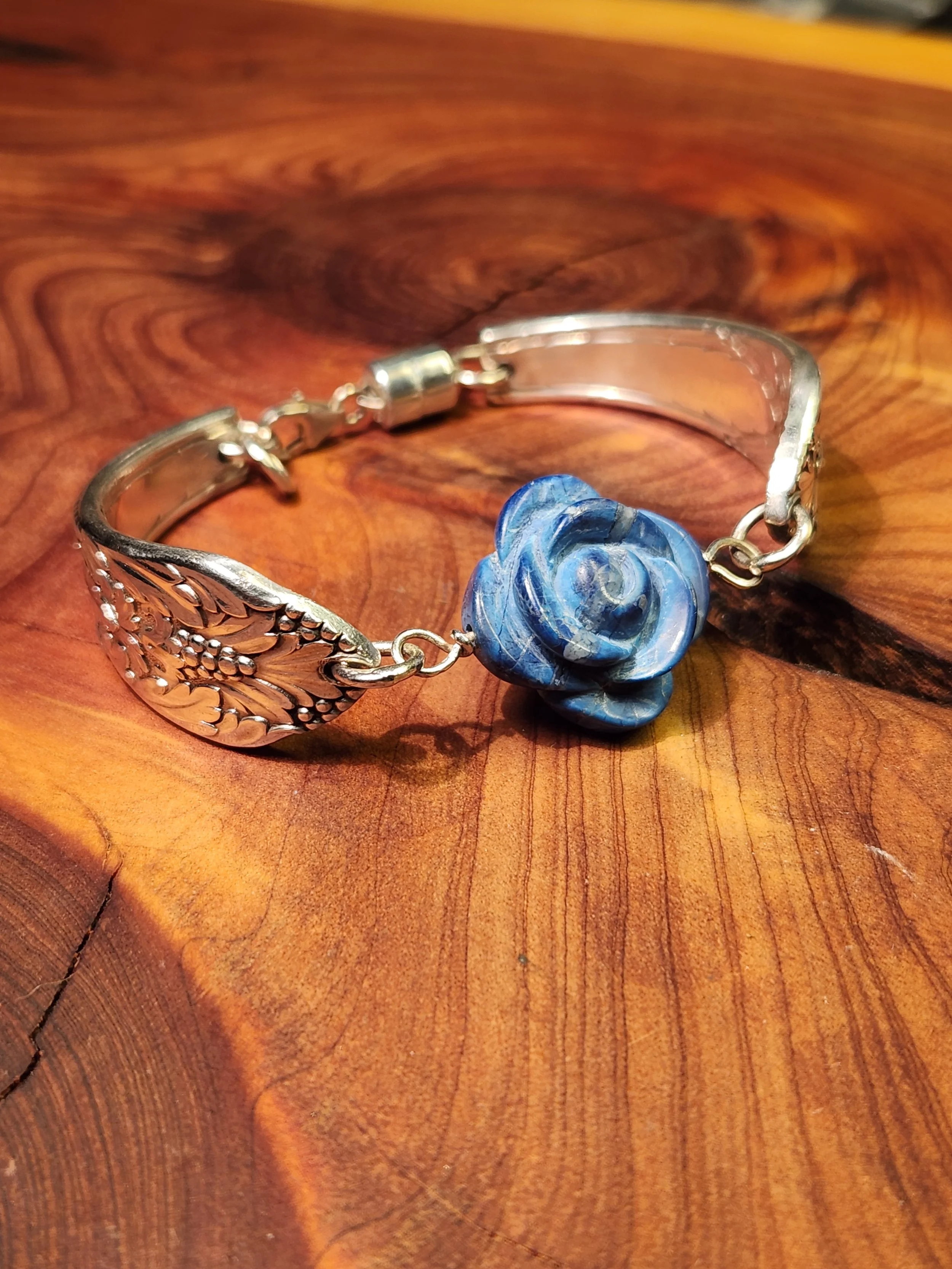 Silver bracelet with blue carved flower charm on a wooden surface.