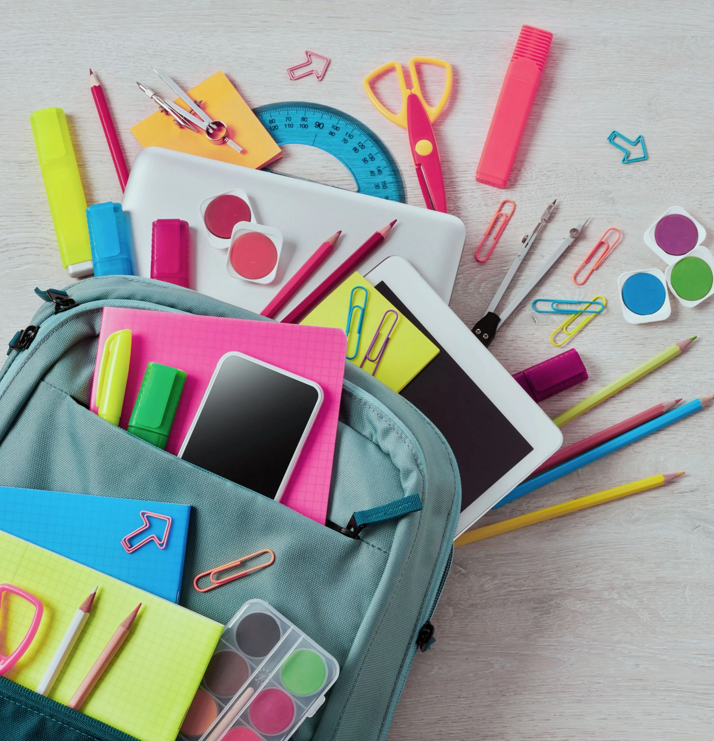 A flatlay of a blue backpack on a table with colorful school supplies spilling out everywhere.