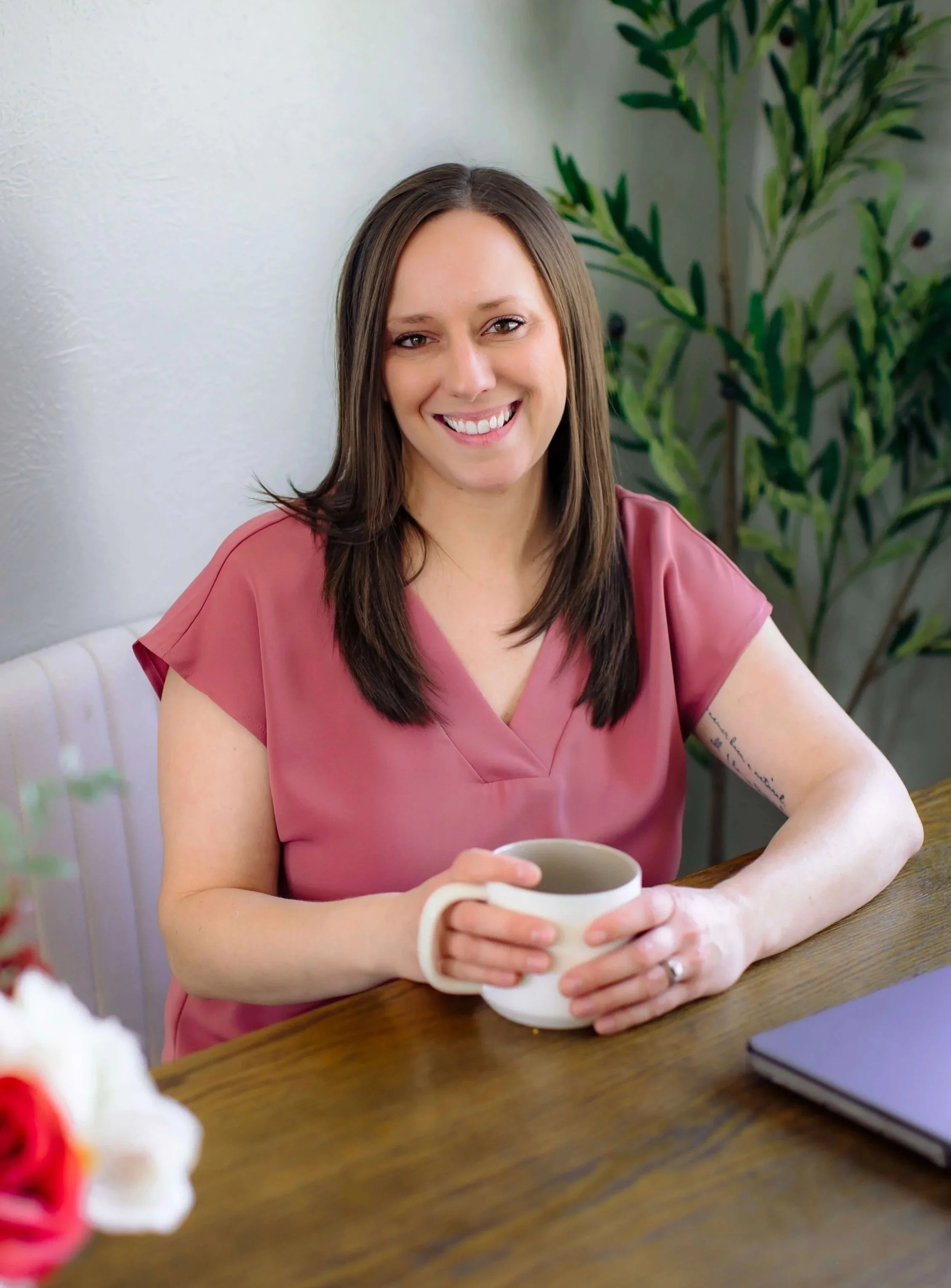 Cassie Roybal, an AuDHD female therapist with brown hair and a pink shirt, sitting at a desk holding a coffee cup and smiling