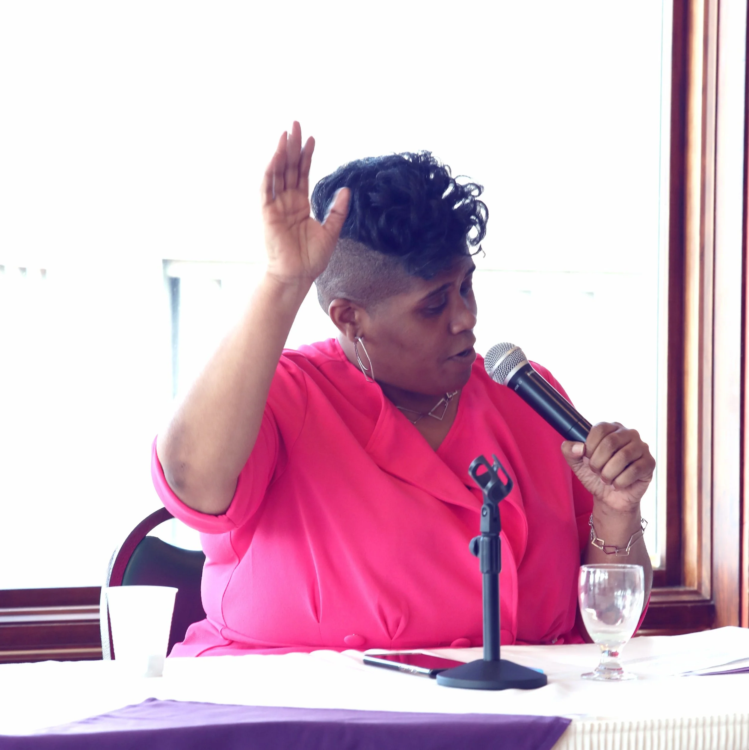 Person in pink jacket speaking into a microphone at a table.