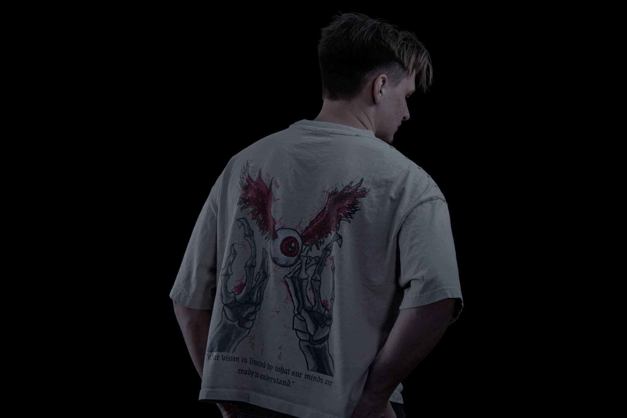 Person with short hair wearing a white t-shirt with a graphic of a dog and a quote on the back, standing against a black background.