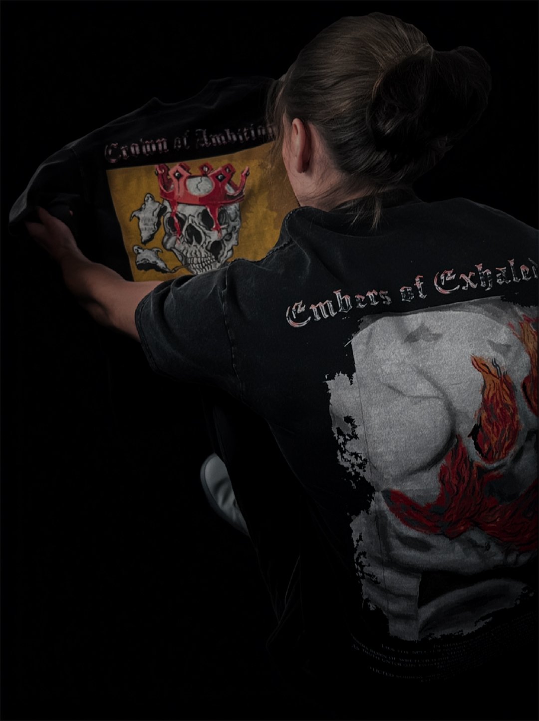 A person with their back to the camera is adjusting a black jacket with logos and graphics, including a skull with a red crown on the back and the inscription "Embers of Calor" on the upper back, against a black background.