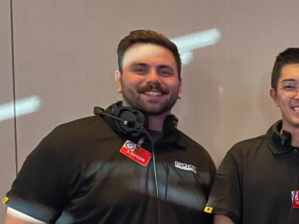 Valley Video team members in black shirts with headphones and visitor badges, standing indoors.