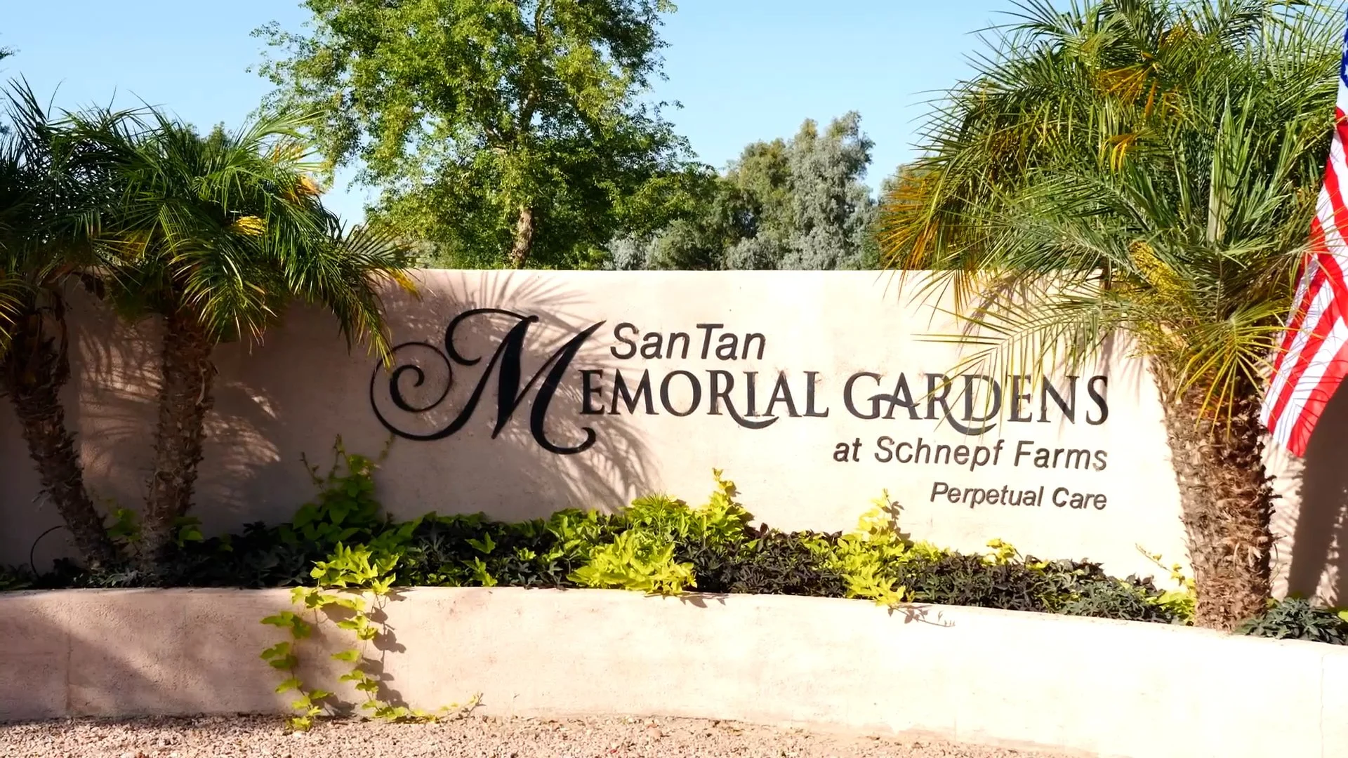 Sign for San Tan Memorial Gardens at Schnepf Farms surrounded by palm trees and greenery.