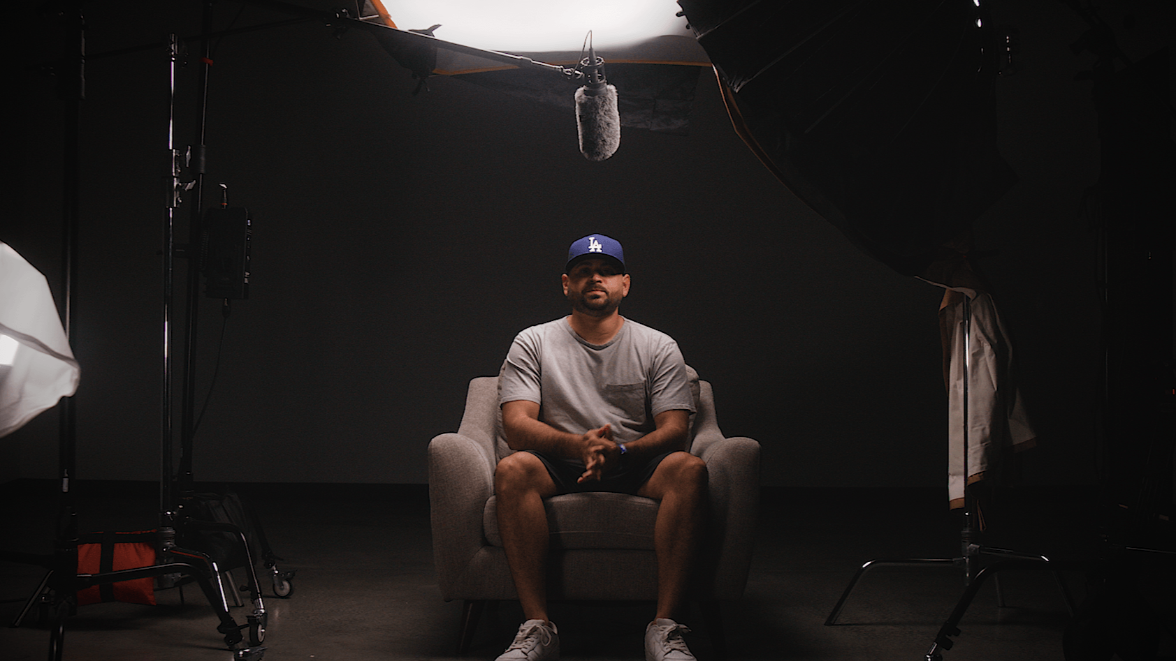 Man sitting on a beige armchair in a photography studio, surrounded by professional lighting and equipment, with dark background.