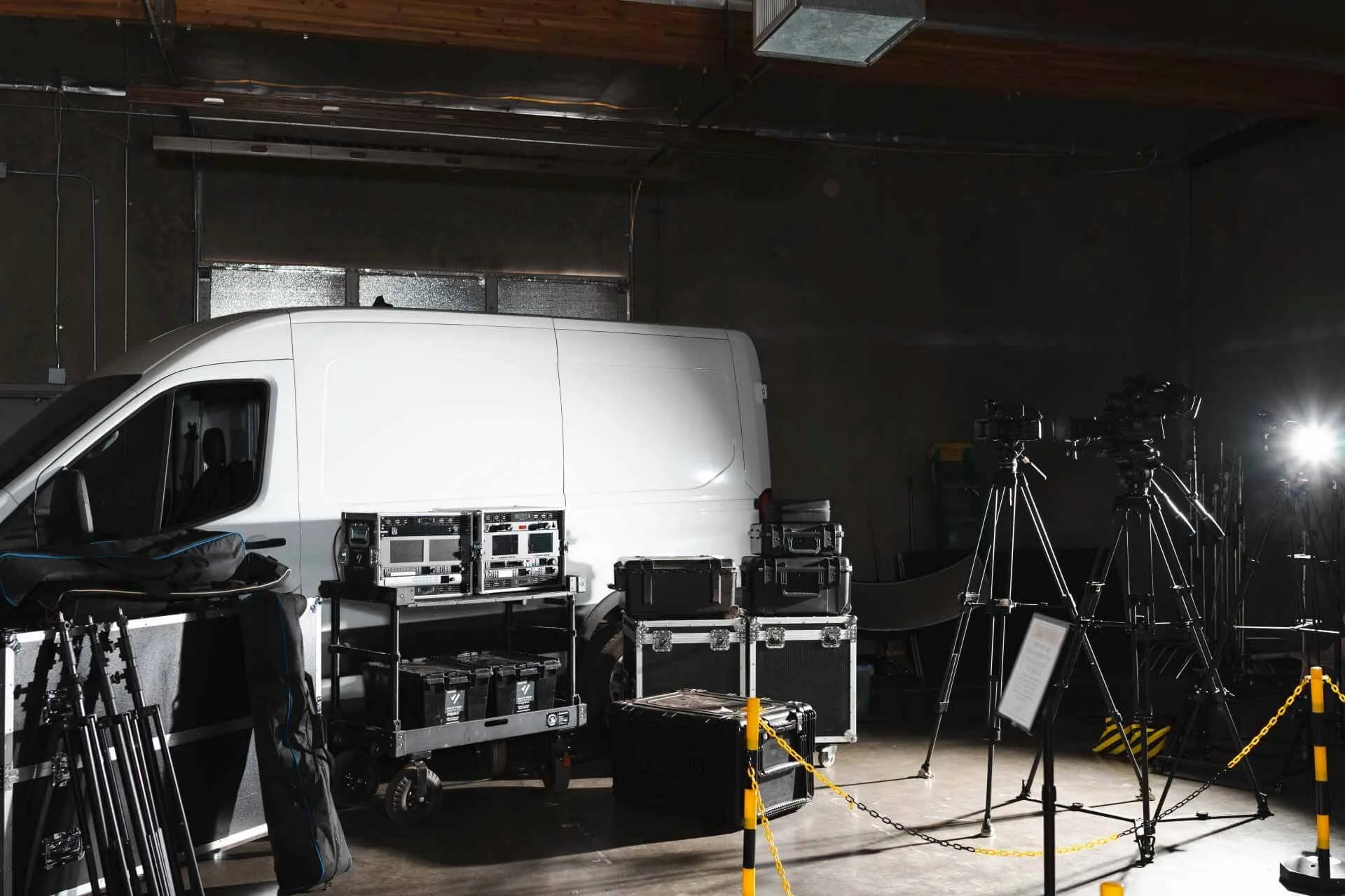 Filming studio with a white van, camera equipment, tripods, and lighting, separated by yellow chains.