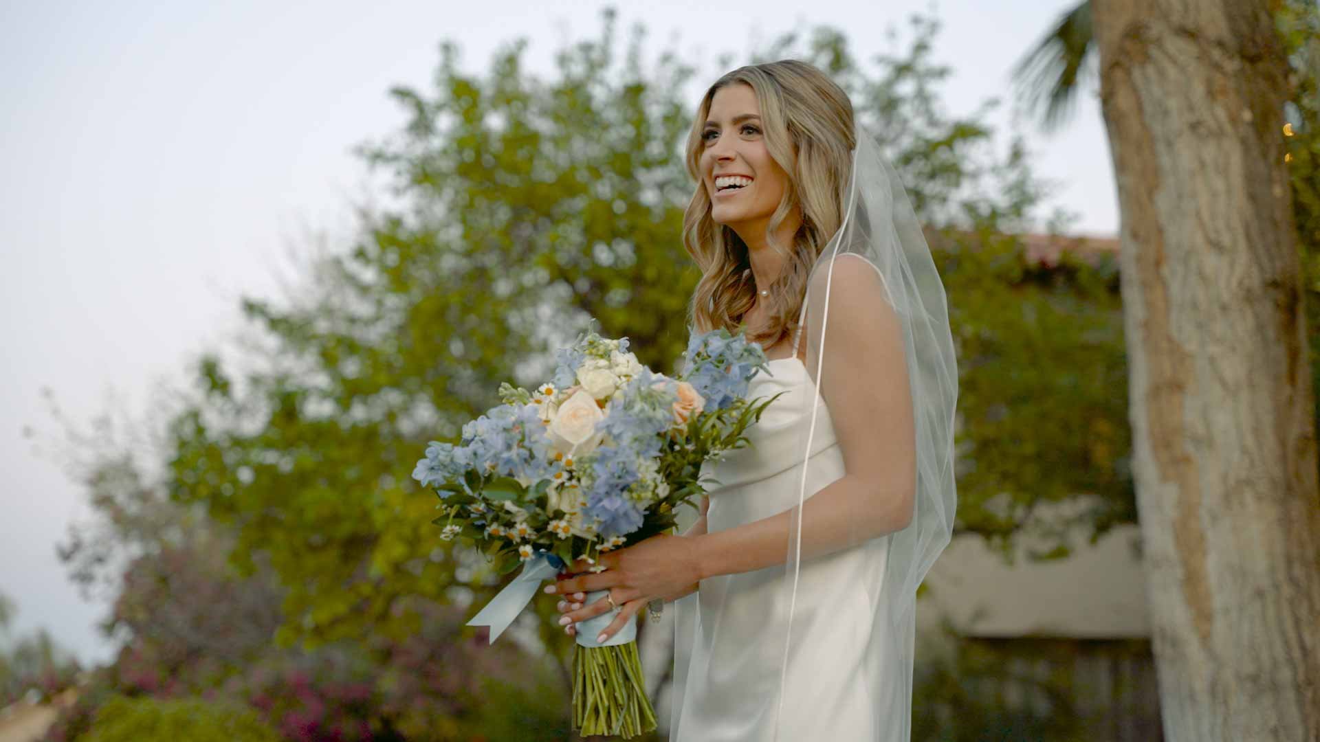 Valley Video wedding videography services. A smiling woman in a white wedding dress holding a bouquet of flowers outdoors.