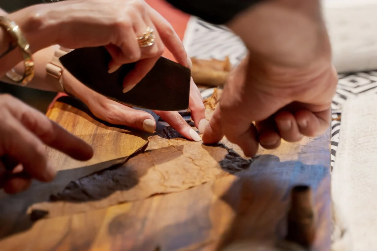 Multiple hands working on repairing or examining a piece of parchment or paper on a wooden surface with tools and pages around.
