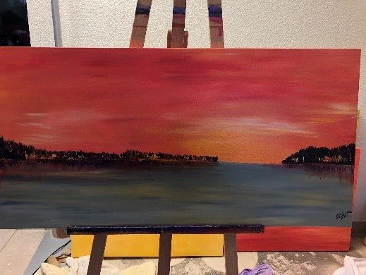 Gemälde einer Landschaft mit rotem Himmel und Wasser, Bäume am Horizont, auf einer Staffelei platziert.