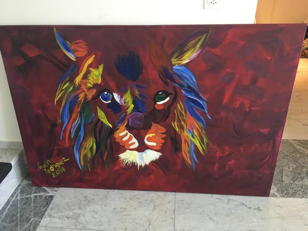 Abstraktes Gemälde eines bunt gefärbten Löwenkopfes auf rotem Hintergrund. Der Löwe hat farbige Strähnen in Blau, Grün, Gelb und Orange.