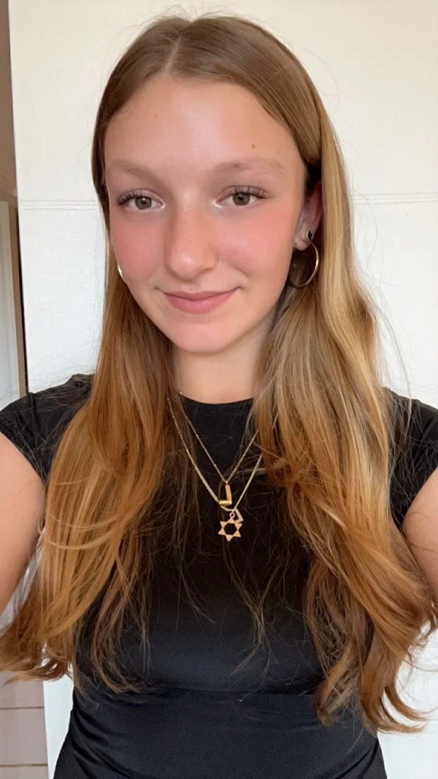 Young woman with long hair wearing a black top and gold necklace.