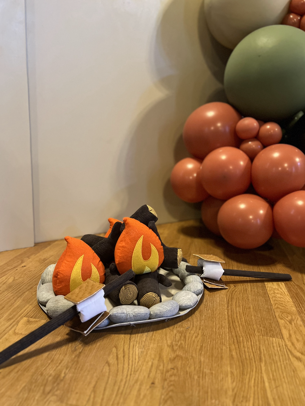A plush toy of a dragon battle axe on a wooden floor near decorative balloon formations.