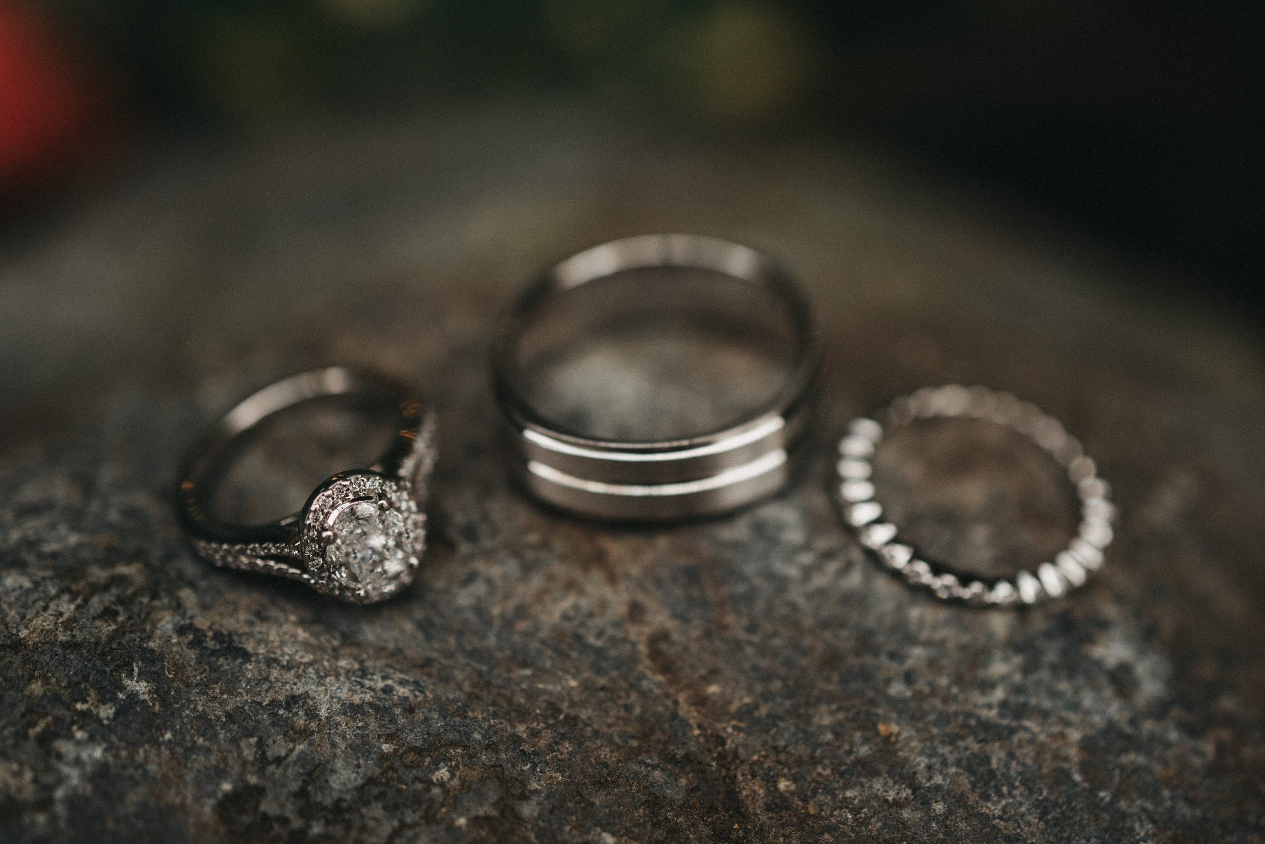 Close-up of three rings on a textured surface: a diamond engagement ring, a plain band, and a ring with small stones