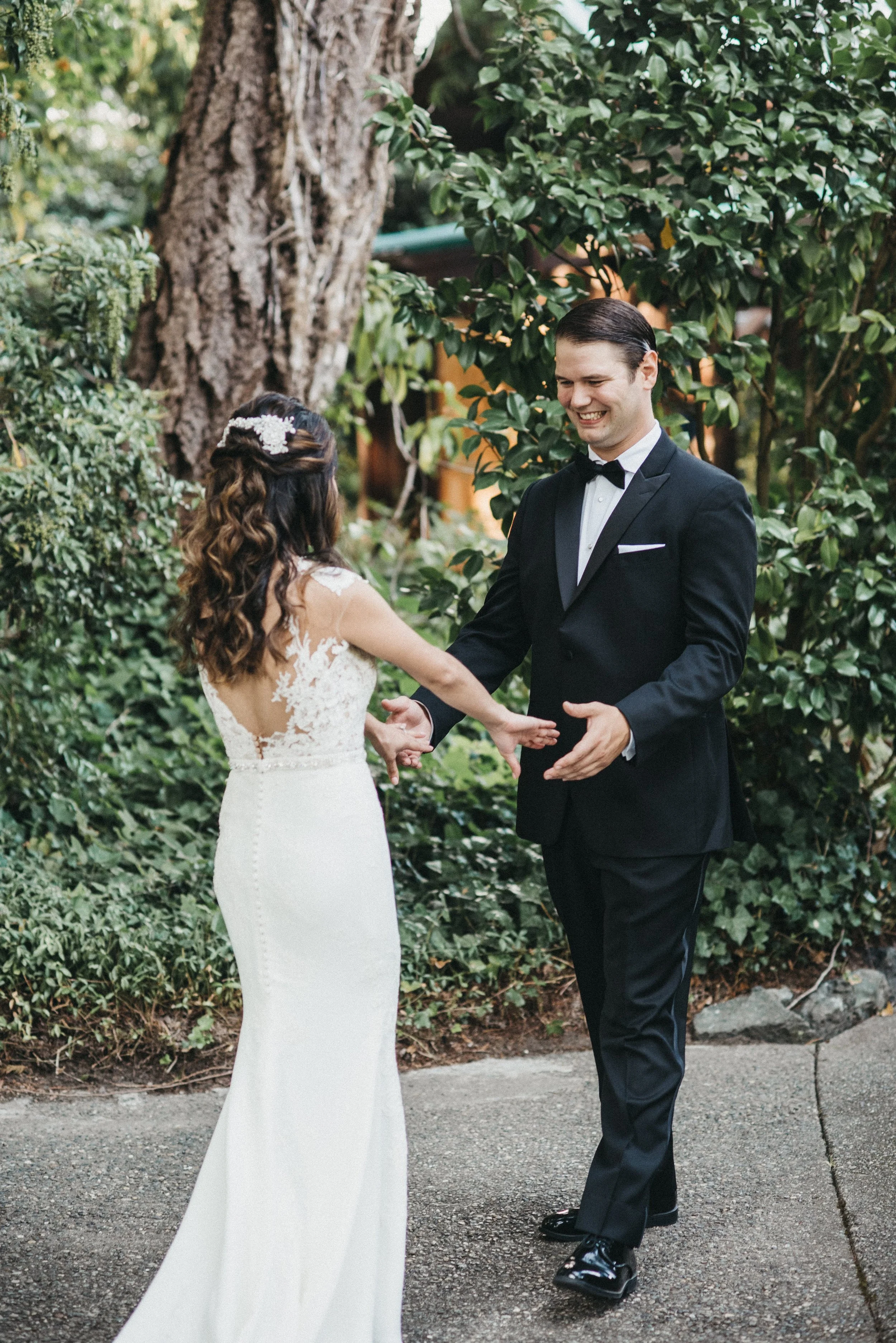 A bride and groom holding hands outside in a garden, smiling at each other during their wedding.