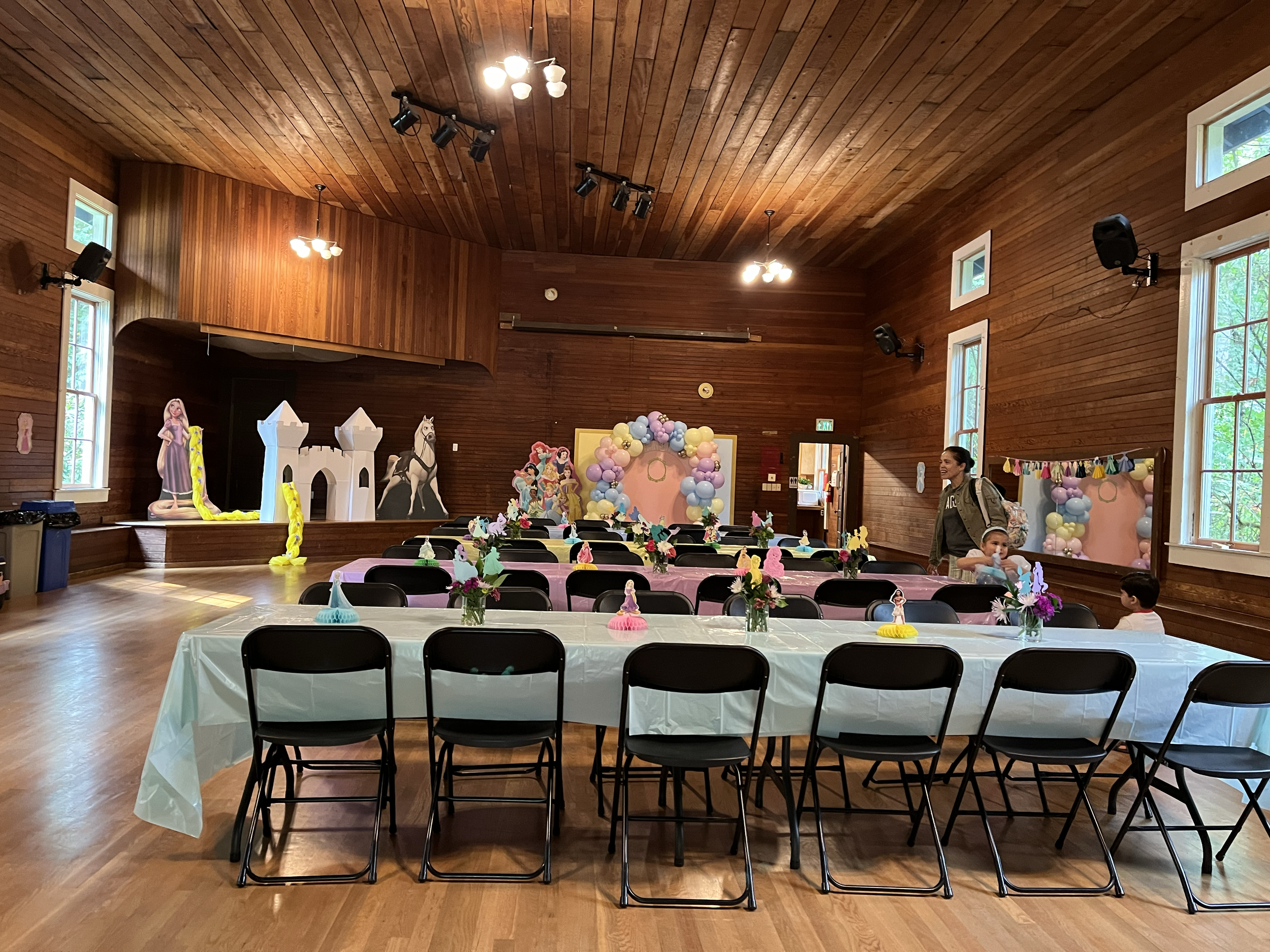 A decorated party room with pink and pastel colors, featuring tables with princess-themed decorations and a castle backdrop for a children's celebration.