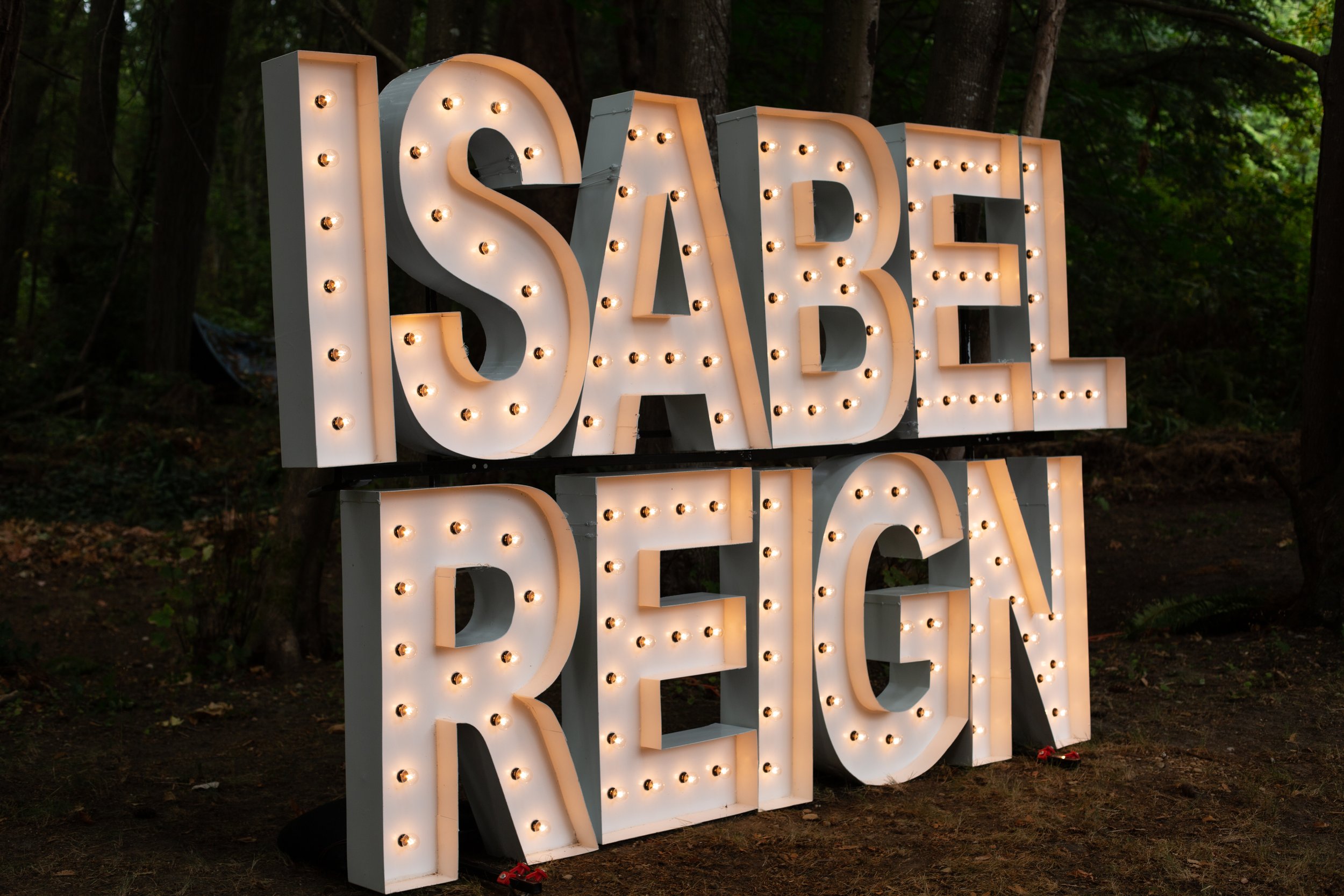Illuminated sign spelling 'SABAL REGEN' with large letters and light bulbs, set outdoors among trees.