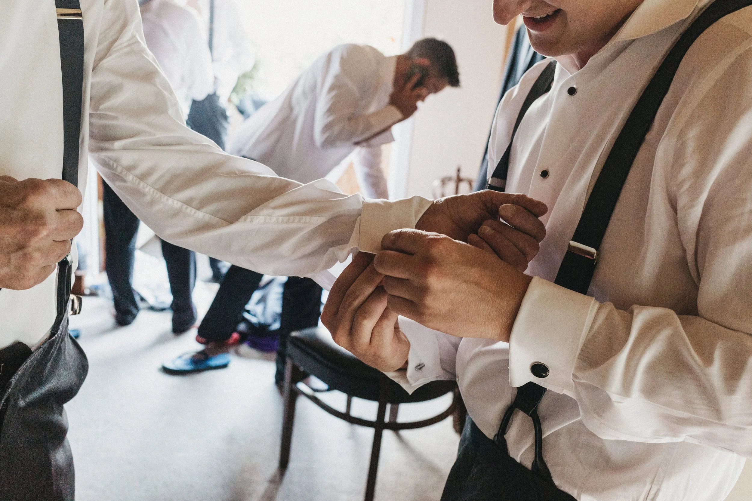 Close-up of a doctor hand putting on a cuff of another doctor in a hospital setting, with a person on the phone in the background.