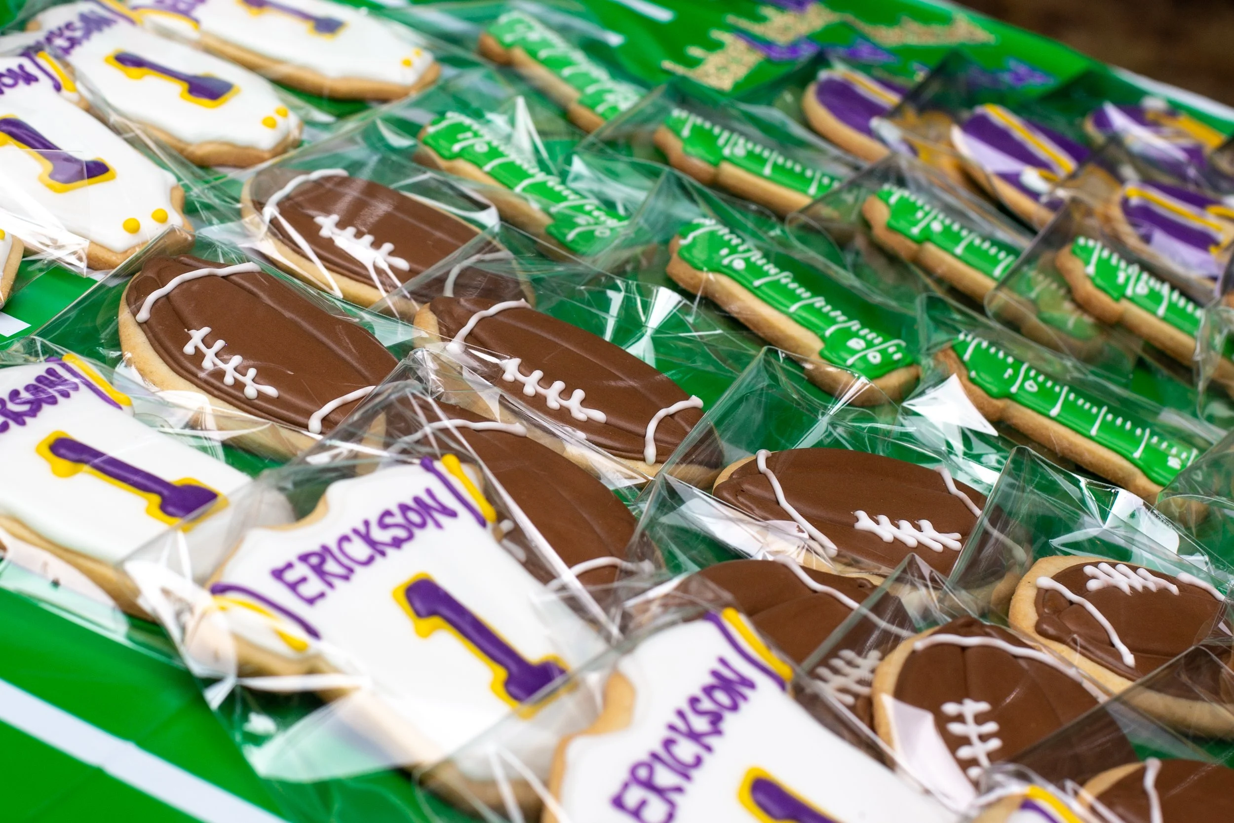 Stacked decorated football-themed cookies in clear plastic wrapping, with personalized cookies displaying names and jersey numbers, likely for a sports celebration.