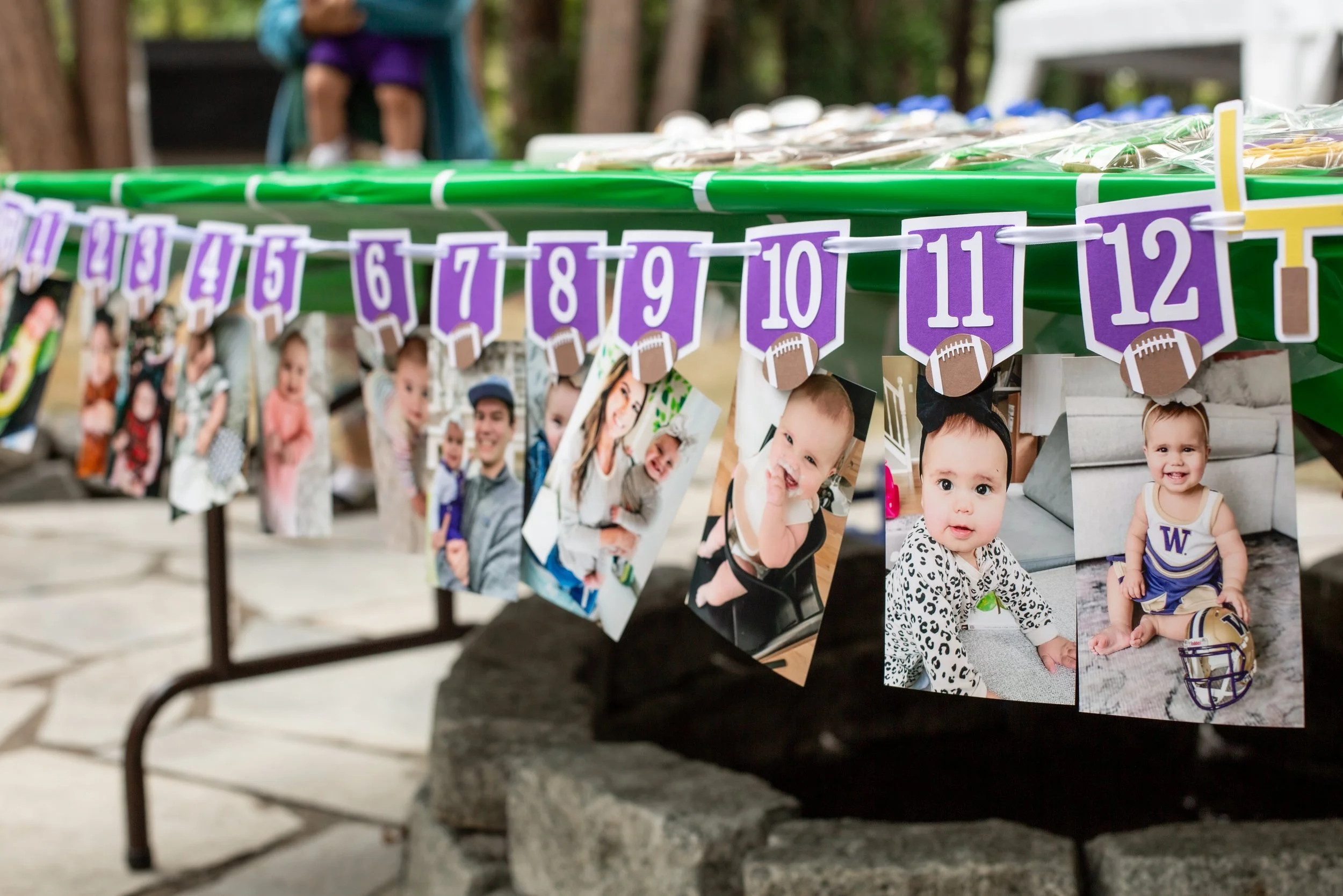 Photographs of children and adults hanging on a string with purple football-shaped and numbered tags, displayed outdoors. The photos include smiling children and a man, suggesting a celebration or event.