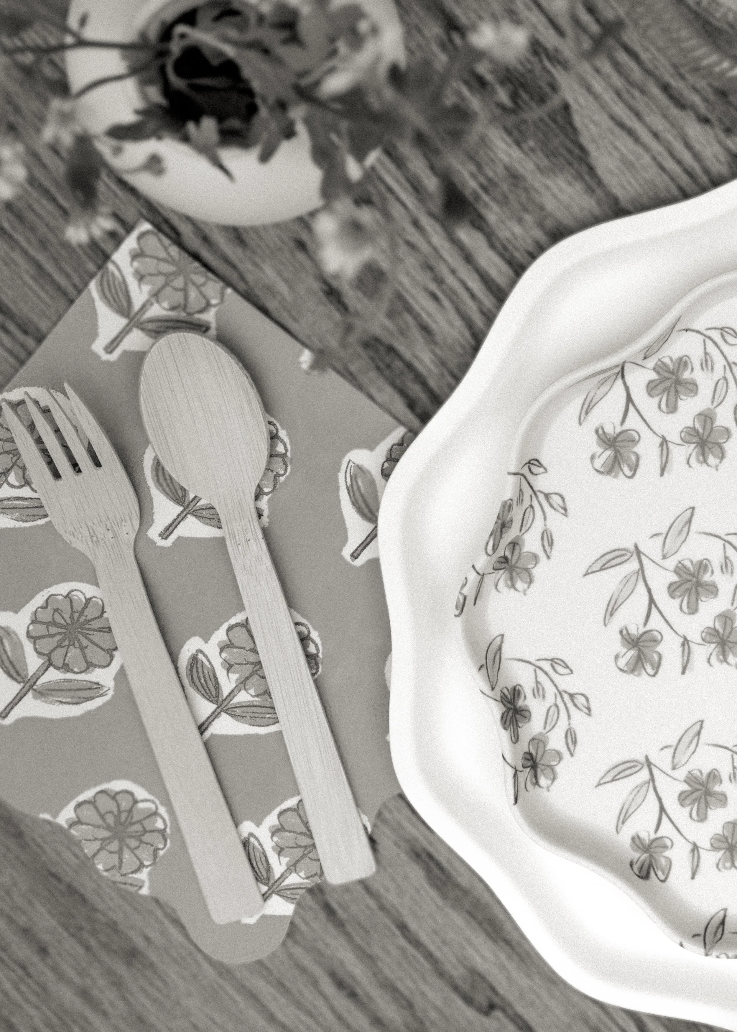 A decorative floral plate, a bowl with floral design, and wooden utensils with floral patterns on handles on a wooden surface.
