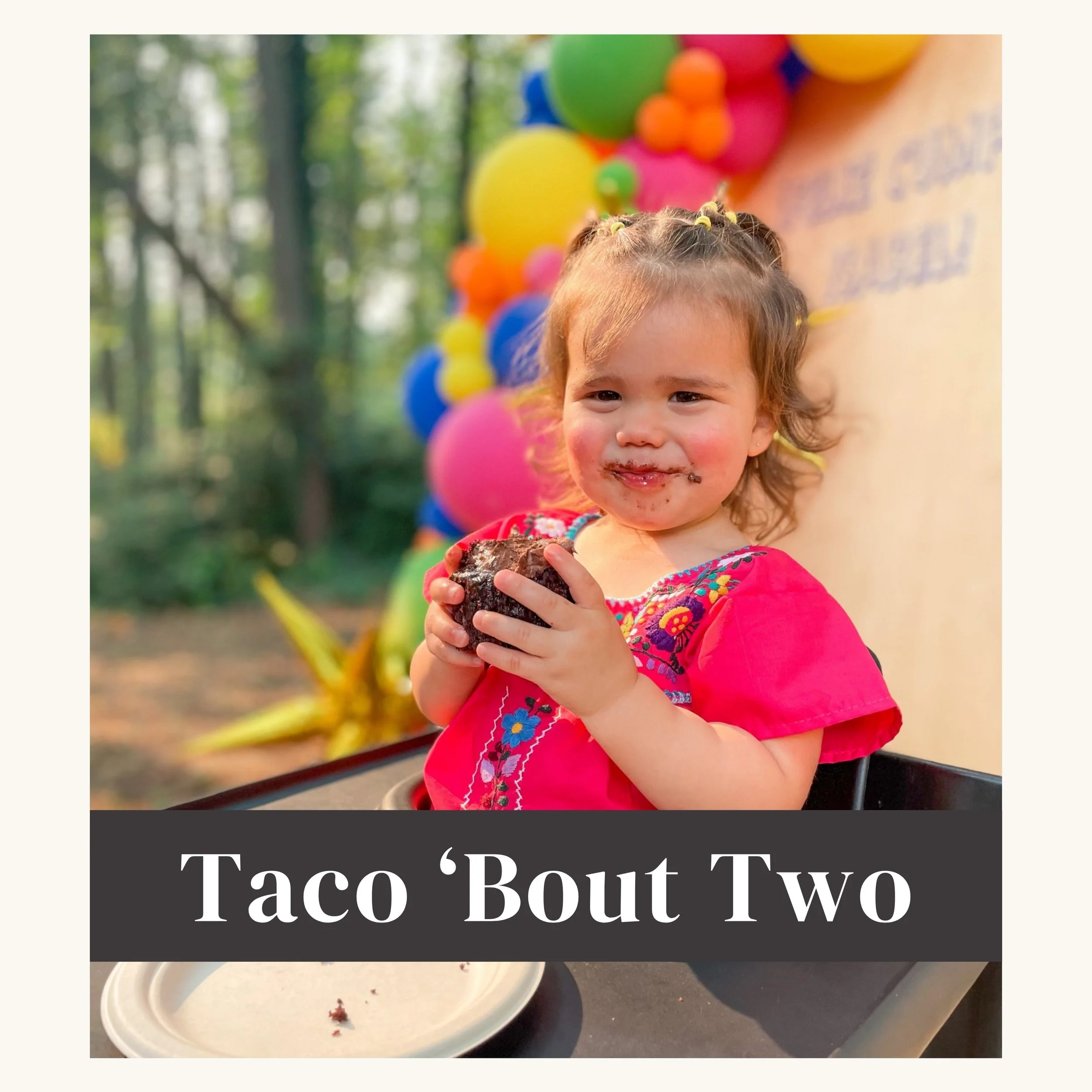 Young girl with a messy face and hands holding a partially eaten chocolate cake, sitting outdoors with colorful balloons in the background, and a sign that reads "Taco 'Bout Two".