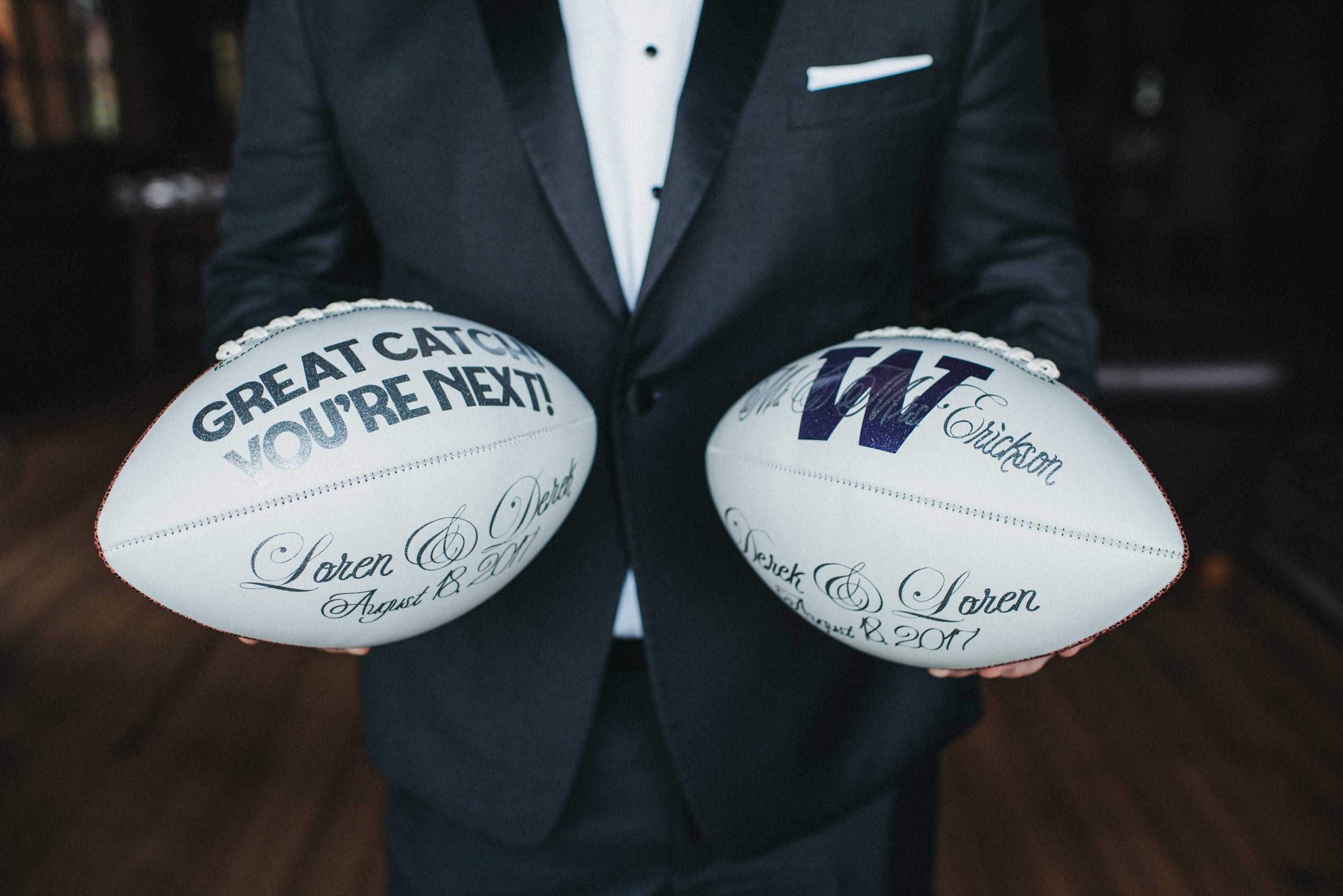 Person in a suit holding two footballs with personalized message and signatures, possibly for a wedding or special event.