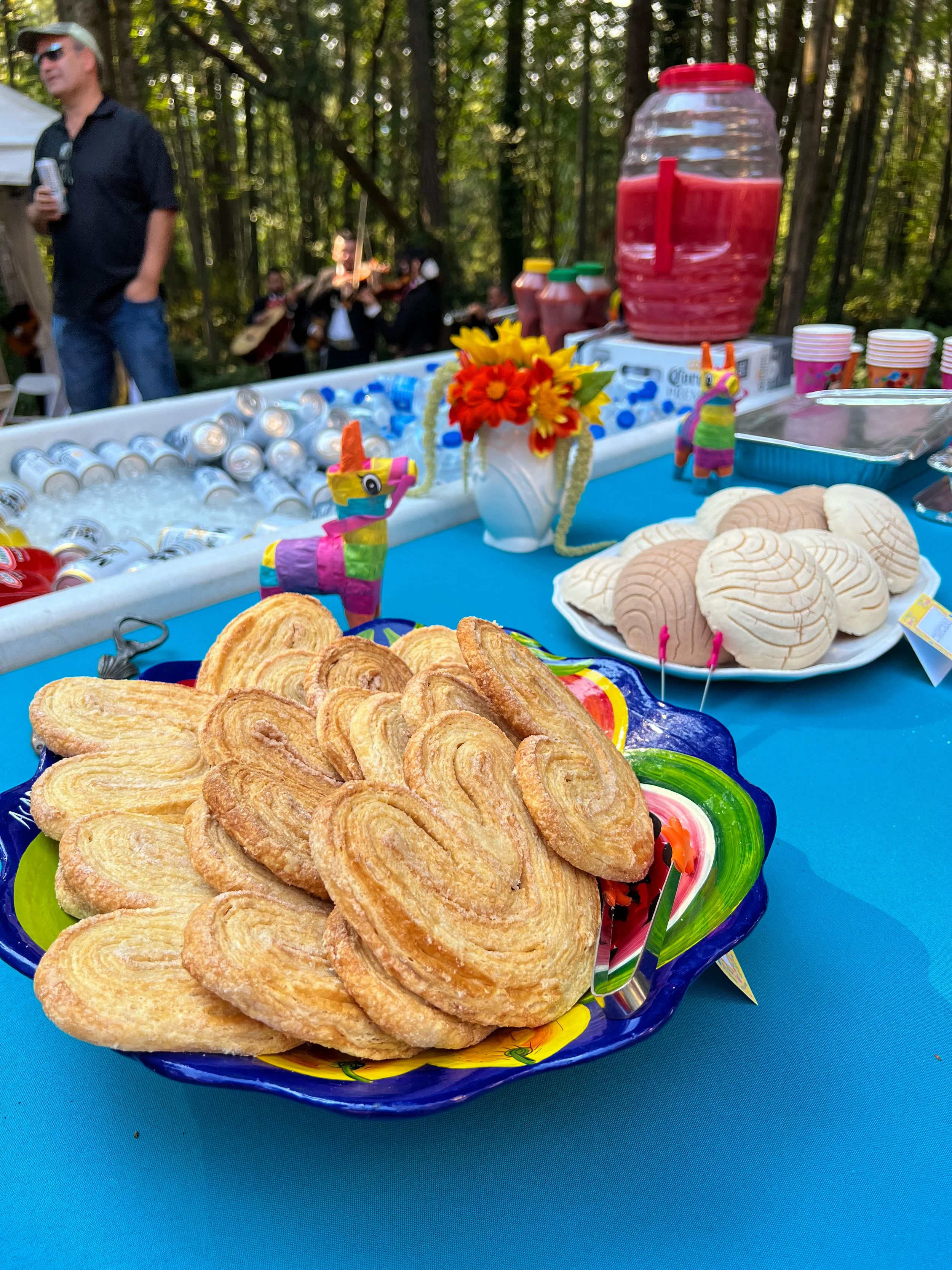 Pastries on a colorful plate at an outdoor celebration table with drinks, cookies, and a piñata in the background.