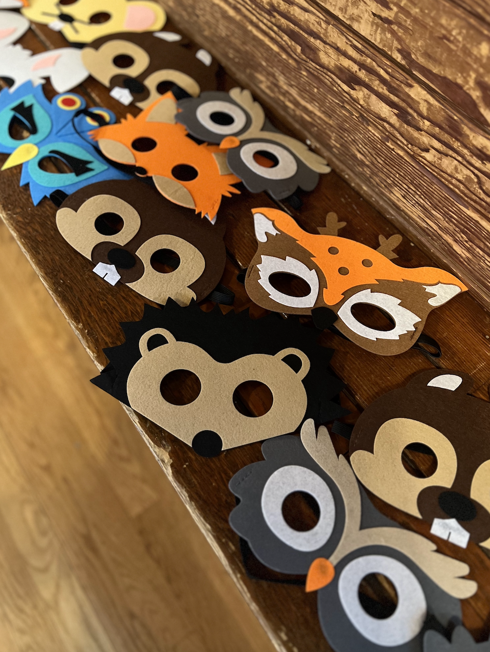 Paper animal masks shaped like a fox, owl, bear, raccoon, and other woodland creatures arranged on a wooden surface.