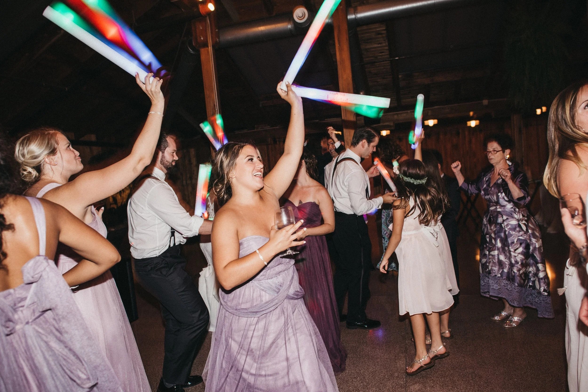 People dancing at a party with glow sticks in a dimly lit room.