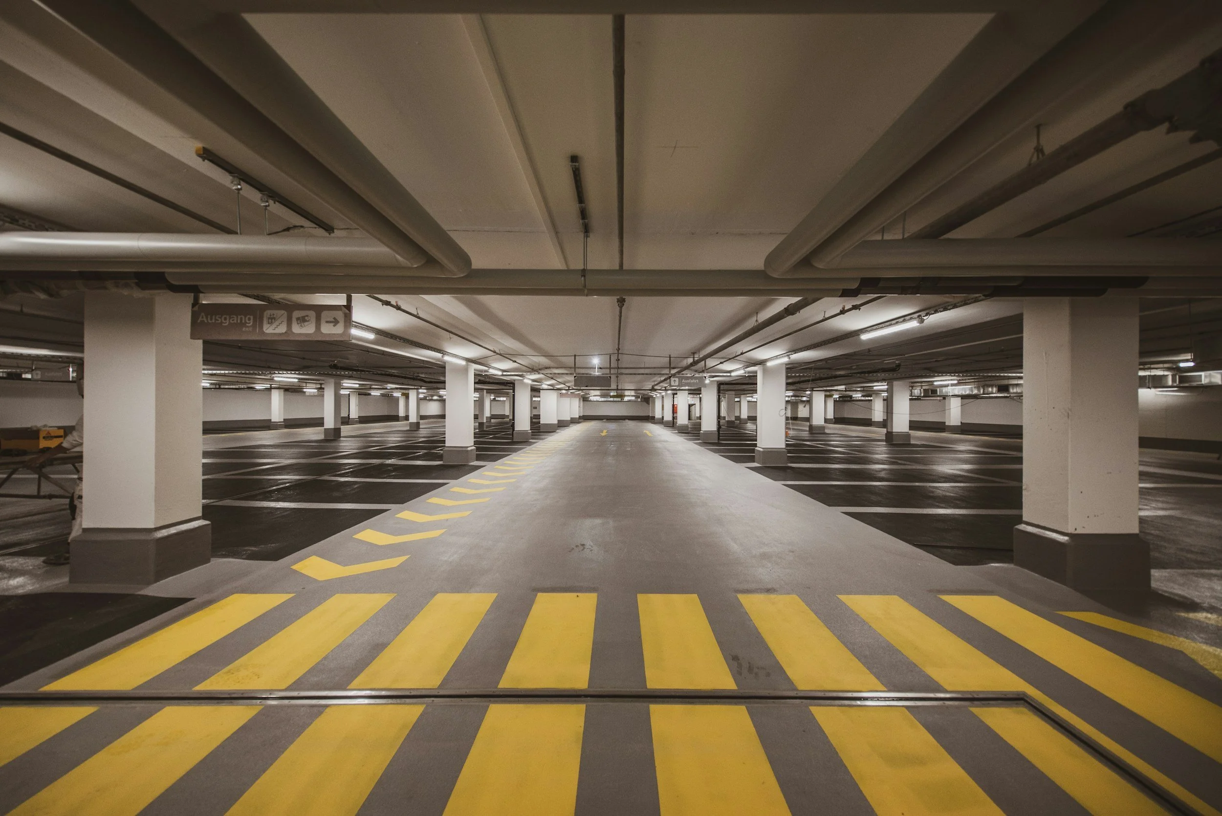 Empty underground parking garage with yellow-striped pedestrian crosswalks and marked parking spots.