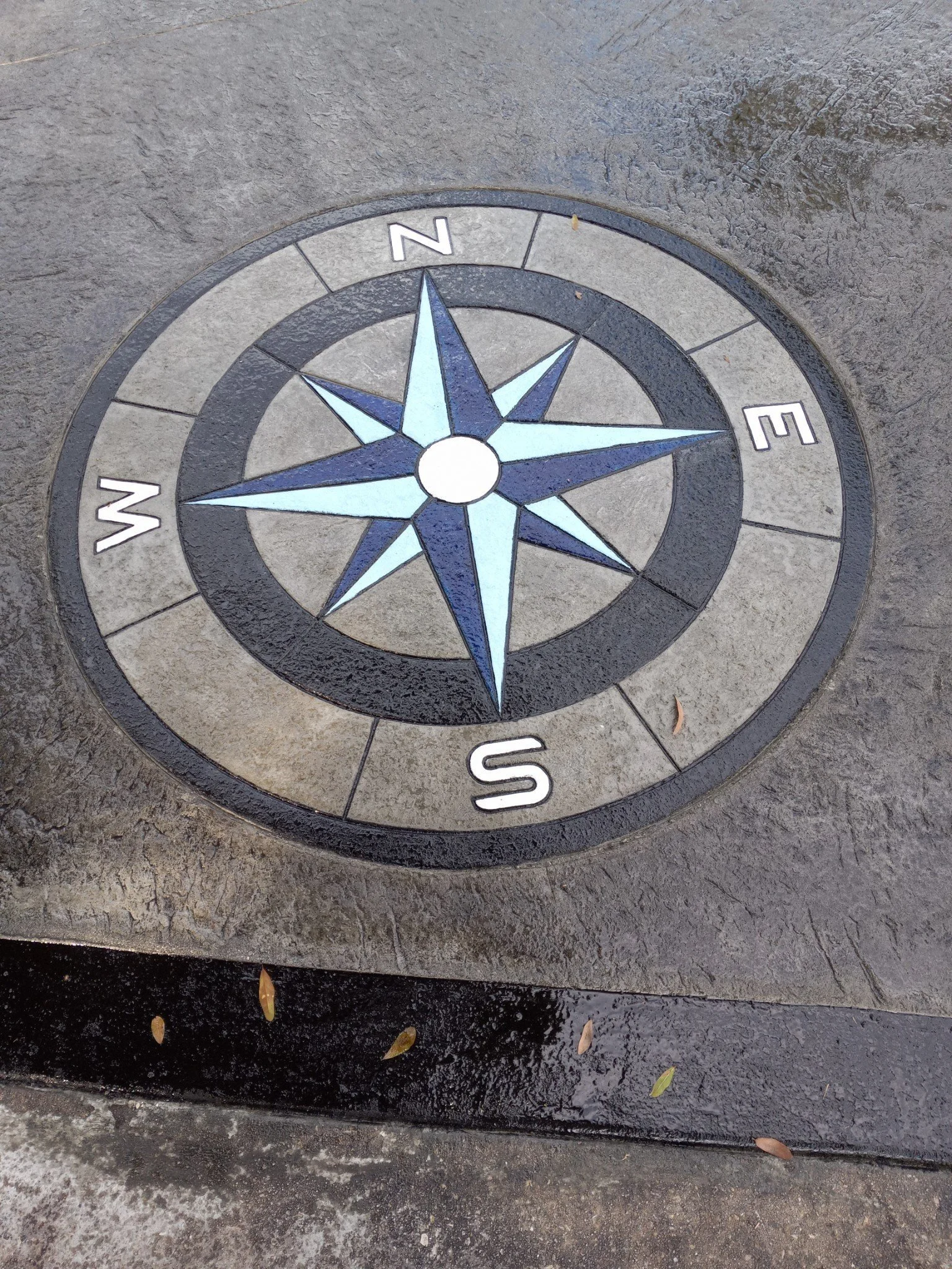 A decorative compass rose embedded in the ground, with the cardinal directions North, East, South, and West labeled.