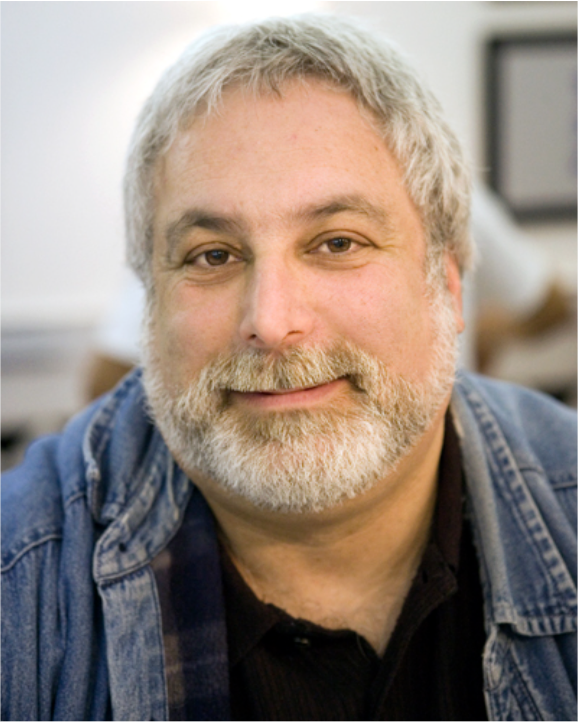 Kenn Rabin headshot smiling with gray hair and beard, wearing a denim shirt.
