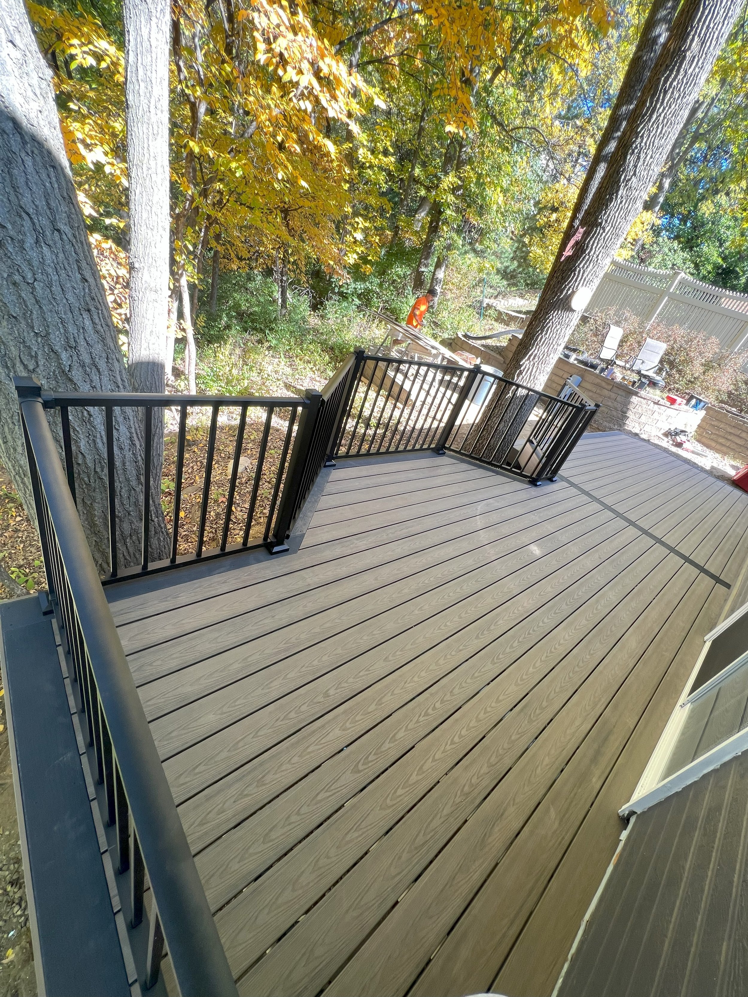 A newly constructed outdoor deck with black metal railings, surrounded by fall foliage and trees.