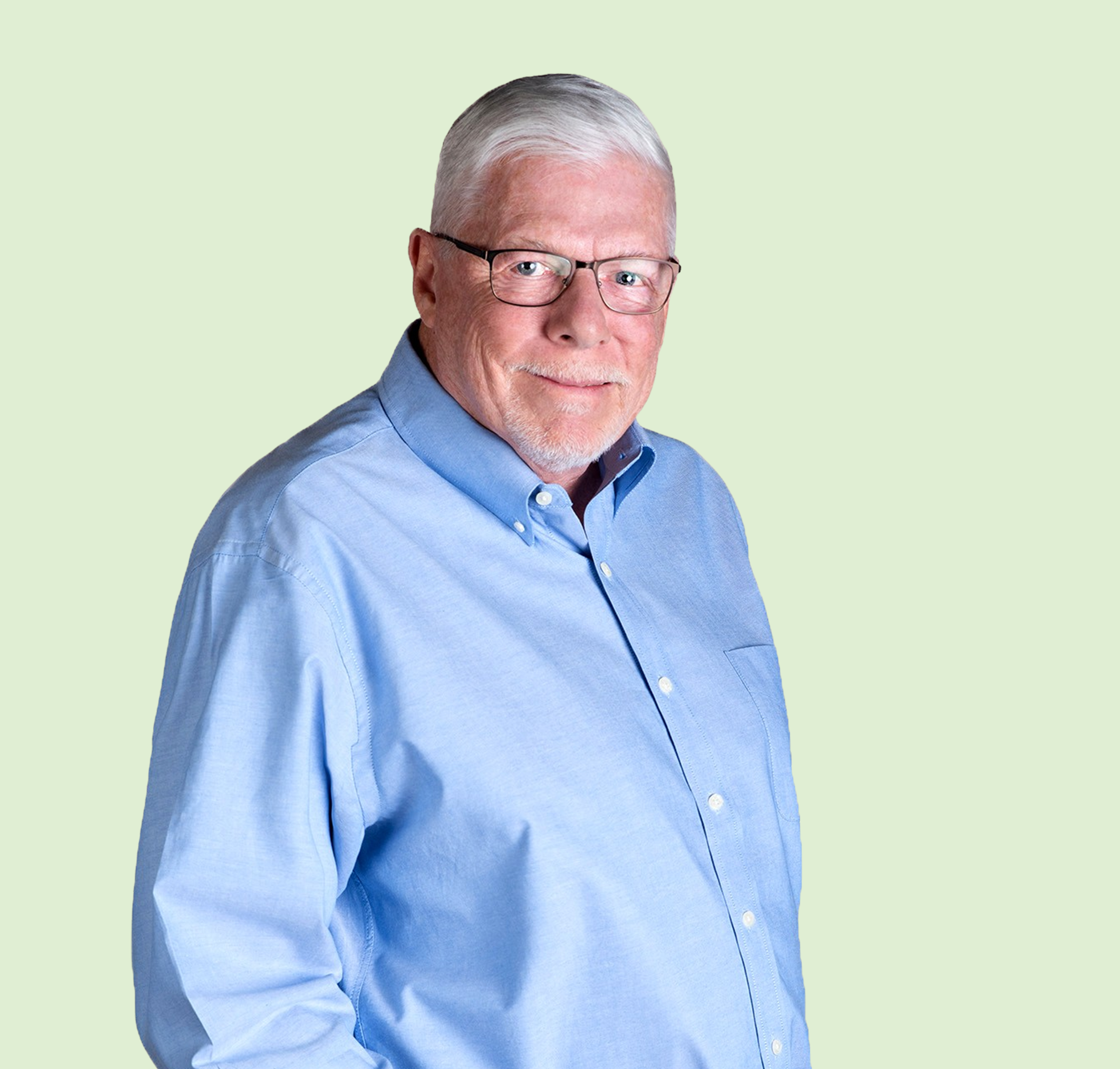 Close-up of an older man with gray hair and glasses, wearing a blue collared shirt, against a light green background.