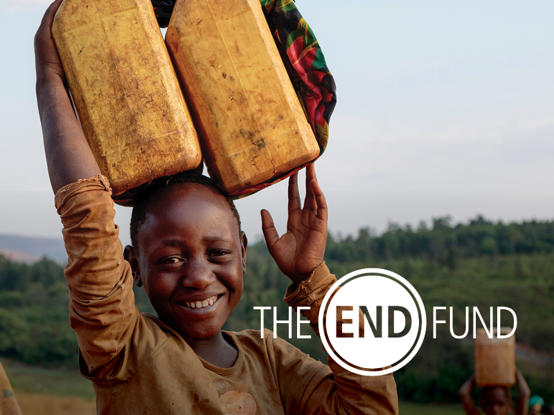 A smiling young boy carrying two large containers on his head outdoors with a rural landscape in the background, and the text 'The End Fund' overlayed on the image.
